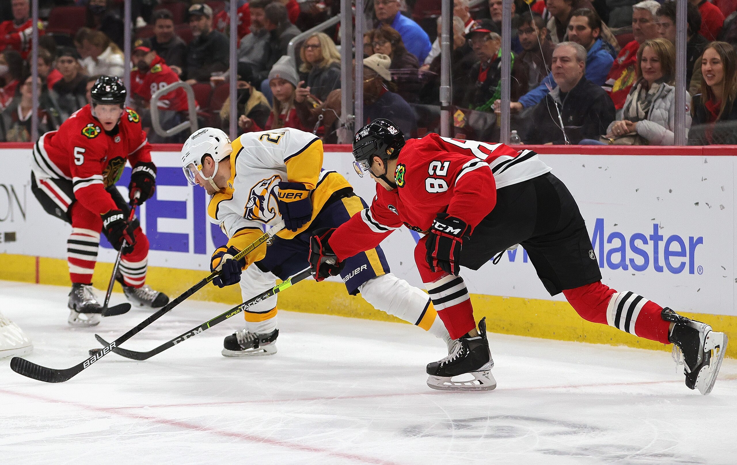 CHICAGO, ILLINOIS - DECEMBER 17: Rocco Grimaldi #23 of the Nashville Predators tries to control the puck between Caleb Jones #82 and Connor Murphy #5 of the Chicago Blackhawks at the United Center on December 17, 2021 in Chicago, Illinois. The Predators defeated the Blackhawks 3-2 in overtime. (Photo by Jonathan Daniel/Getty Images) CHICAGO, ILLINOIS - DECEMBER 17: Rocco Grimaldi #23 of the Nashville Predators tries to control the puck between Caleb Jones #82 and Connor Murphy #5 of the Chicago Blackhawks at the United Center on December 17, 2021 in Chicago, Illinois. The Predators defeated the Blackhawks 3-2 in overtime. (Photo by Jonathan Daniel/Getty Images)