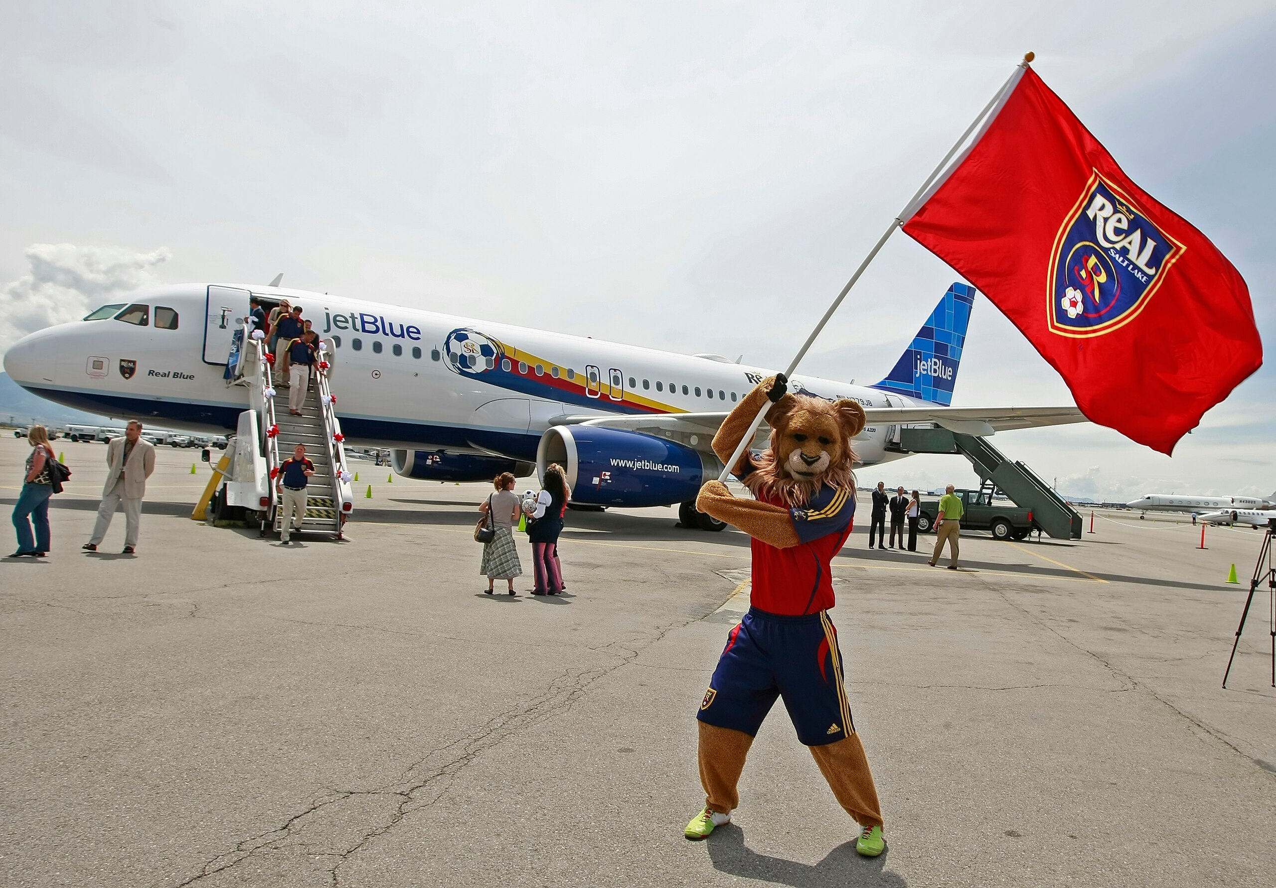 SALT LAKE CITY, UT - JUNE 12: Real Salt Lake's mascot Leonardo The Lion waves a flag in front of a Jet Blue plane branded with the Real Salt Lake Logo and name at the Salt Lake International Airport  June 12, 2009 in Salt Lake City, Utah. Real is the first American major soccer team to have a plane branded with it's name a logo.  (Photo by George Frey/MLS via Getty Images)
