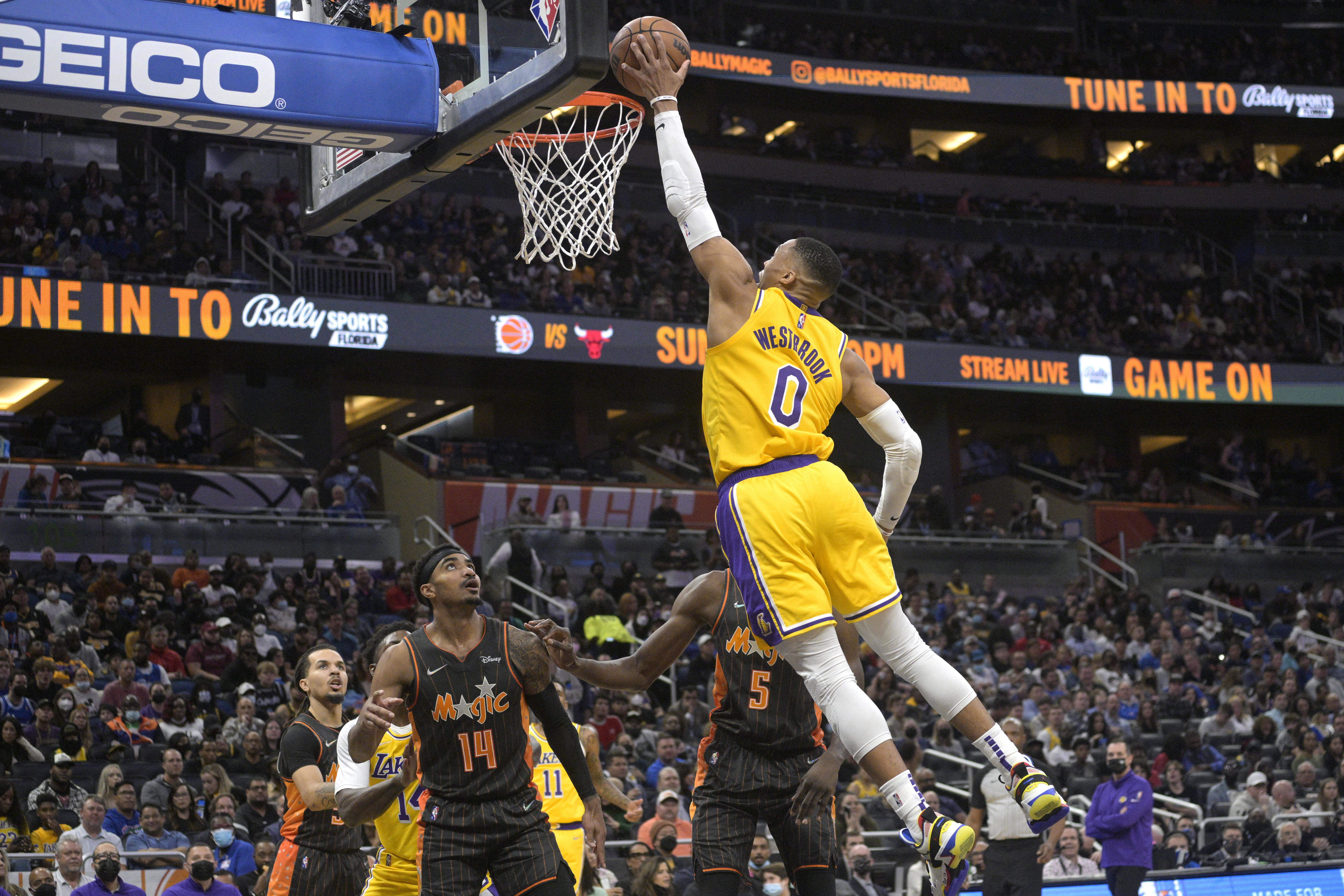 Los Angeles Lakers guard Russell Westbrook (0) goes up for a dunk in front of Orlando Magic guard Gary Harris (14) and center Mo Bamba (5) during the first half of an NBA basketball game, Friday, Jan. 21, 2022, in Orlando, Fla. (AP Photo/Phelan M. Ebenhack)