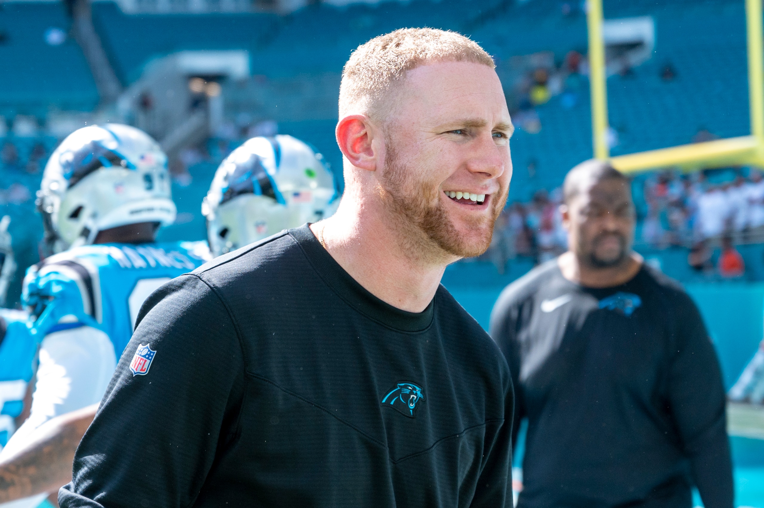 Carolina Panthers offensive coordinator Joe Brady smiles as he greets players on the field before an NFL football game against the Miami Dolphins, Sunday, Nov. 28, 2021, in Miami Gardens, Fla. (AP Photo/Doug Murray)