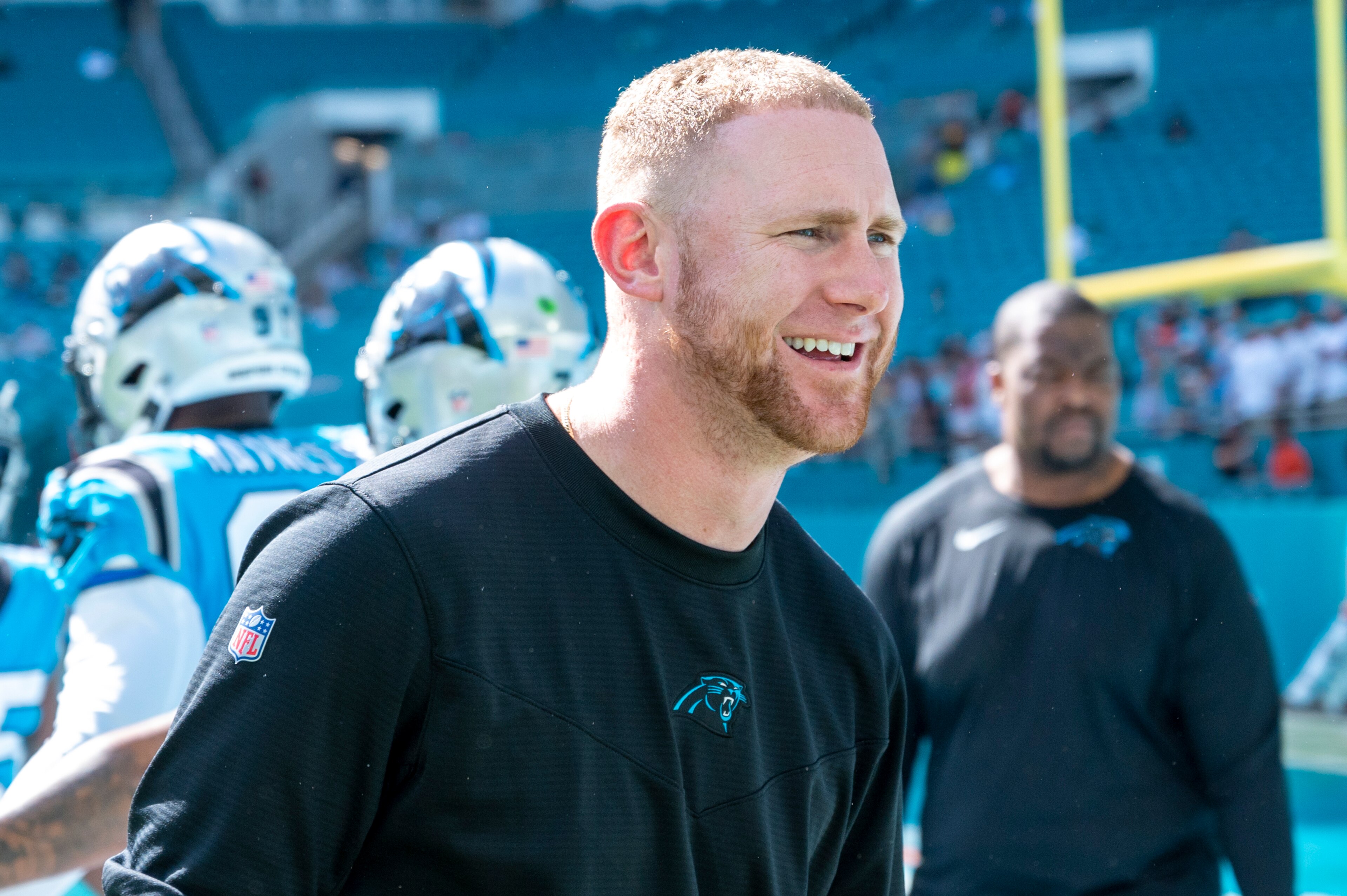 Carolina Panthers offensive coordinator Joe Brady smiles as he greets players on the field before an NFL football game against the Miami Dolphins, Sunday, Nov. 28, 2021, in Miami Gardens, Fla. (AP Photo/Doug Murray)