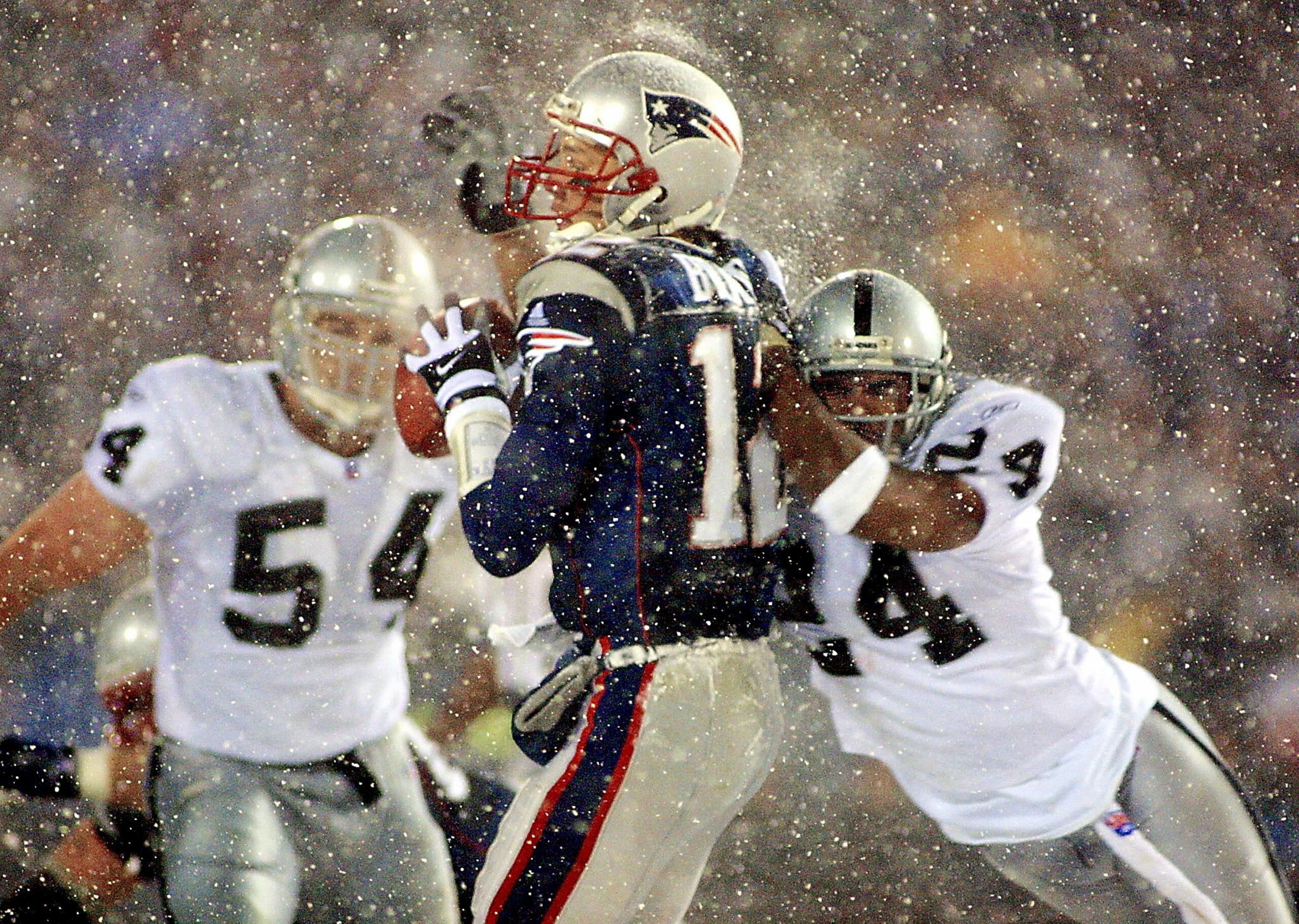 New England Patriots quarterback Tom Brady (C) takes a hit from Charles Woodson (R) of the Oakland Raiders on a pass attempt in the last two minutes of the game in their AFC playoff 19 January 2002 in Foxboro, Massachusetts. The Patriots won 16-13 in overtime. AFP PHOTO/Matt CAMPBELL (Photo by MATT CAMPBELL / AFP) (Photo by MATT CAMPBELL/AFP via Getty Images) New England Patriots quarterback Tom Brady (C) takes a hit from Charles Woodson (R) of the Oakland Raiders on a pass attempt in the last two minutes of the game in their AFC playoff 19 January 2002 in Foxboro, Massachusetts. The Patriots won 16-13 in overtime. AFP PHOTO/Matt CAMPBELL (Photo by MATT CAMPBELL / AFP) (Photo by MATT CAMPBELL/AFP via Getty Images)