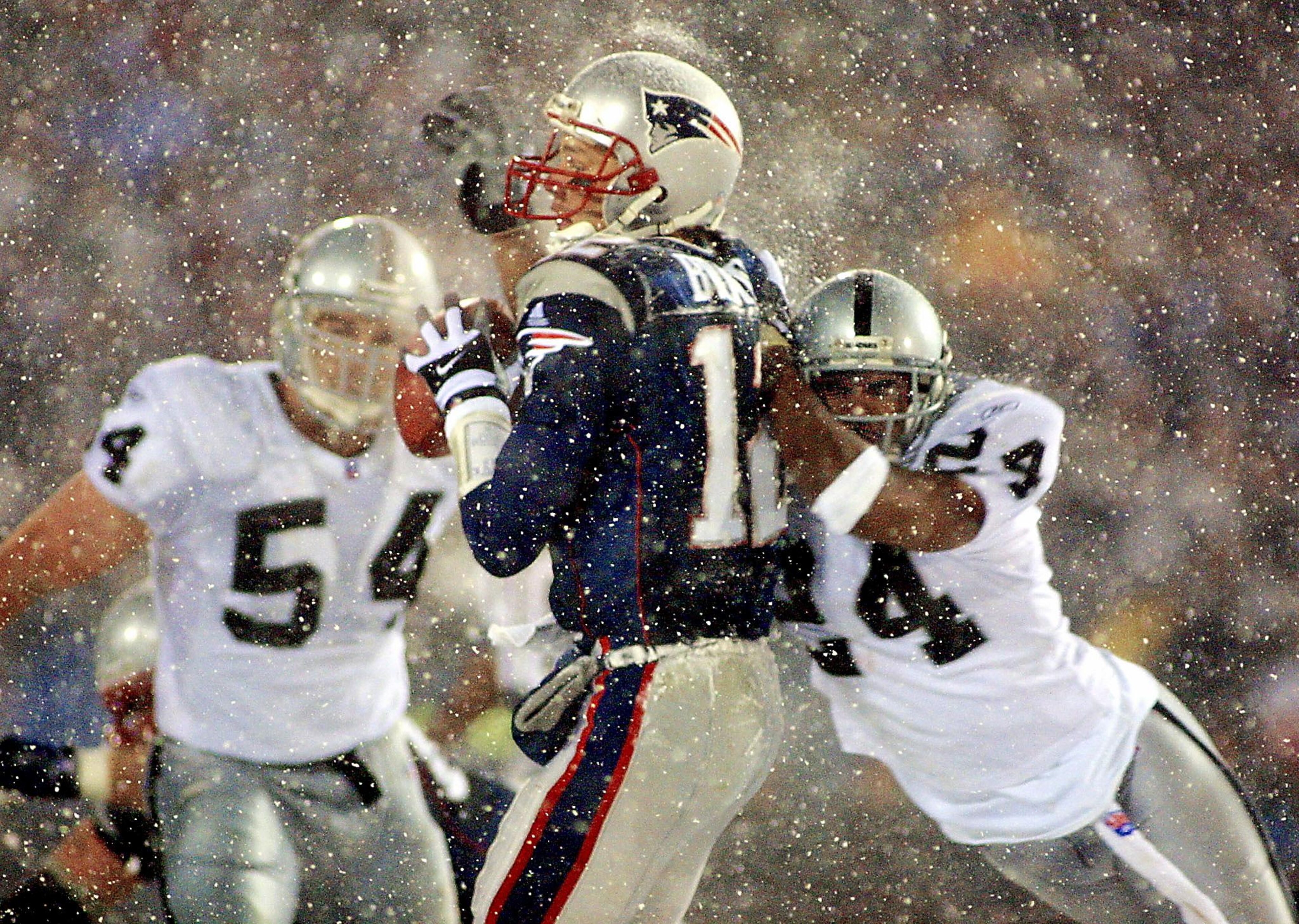 New England Patriots  quarterback Tom Brady (C) takes a hit from Charles Woodson (R) of the Oakland Raiders on a pass attempt in the last two minutes of the game in their AFC playoff 19 January 2002 in Foxboro, Massachusetts.  The Patriots won 16-13 in overtime. AFP PHOTO/Matt CAMPBELL (Photo by MATT CAMPBELL / AFP) (Photo by MATT CAMPBELL/AFP via Getty Images)