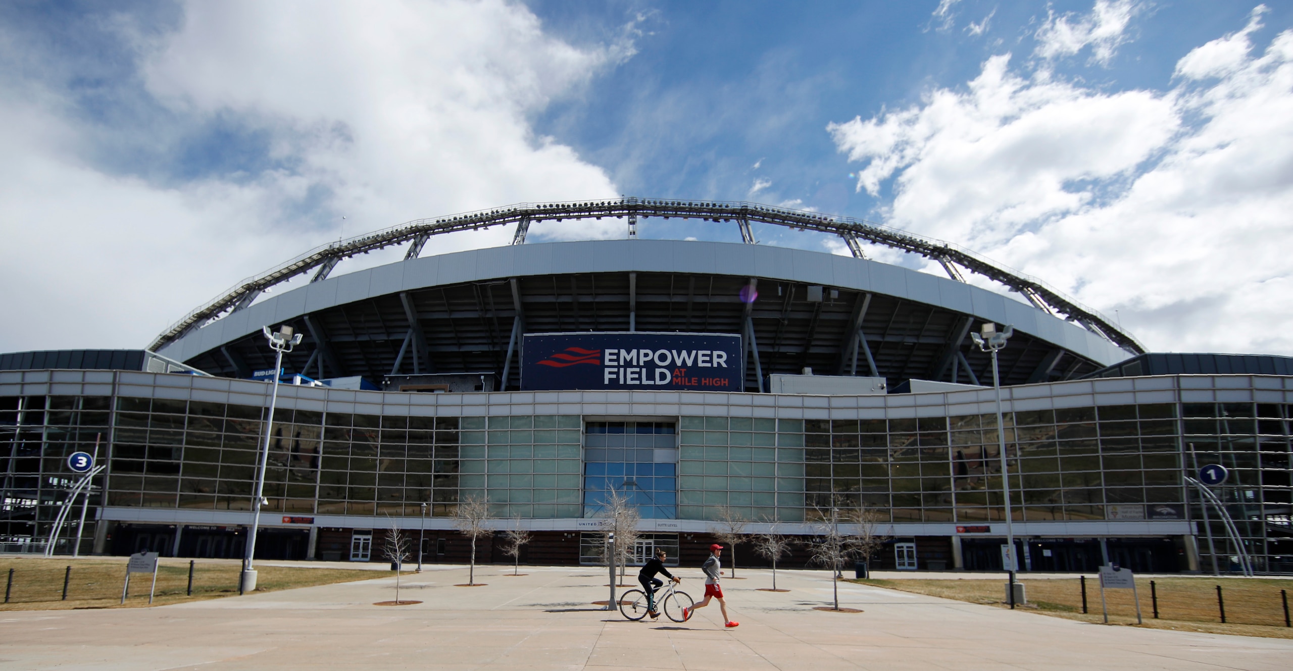 A runner and bicyclist circle Mile High Stadium for exercise with gymnasiums closed because of the spread of coronavirus Sunday, March 22, 2020, in Denver. According to the World Health Organization, most people recover in about three to six weeks depending on the severity of the COVID-19 illness. (AP Photo/David Zalubowski)