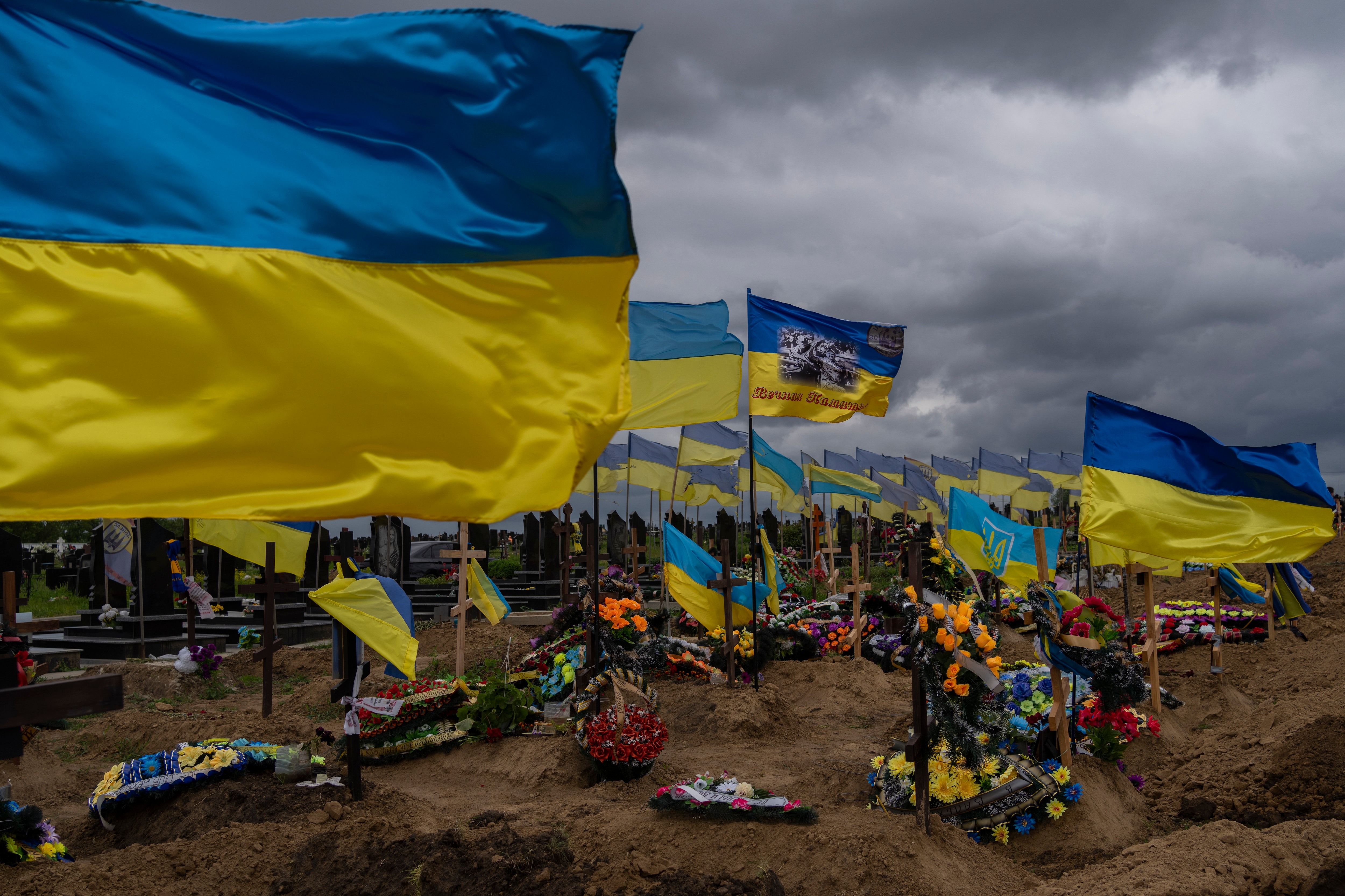 FILe - Ukrainian flags flutter atop graves of fallen soldiers in Kharkiv cemetery, eastern Ukraine, Sunday, May 22, 2022. Americans are becoming less supportive of punishing Russia for launching its invasion of Ukraine if it comes at the expense of the U.S. economy, a sign of rising anxiety over inflation and other challenges. That's according to a new poll from The Associated Press-NORC Center for Public Affairs Research. (AP Photo/Bernat Armangue, File)