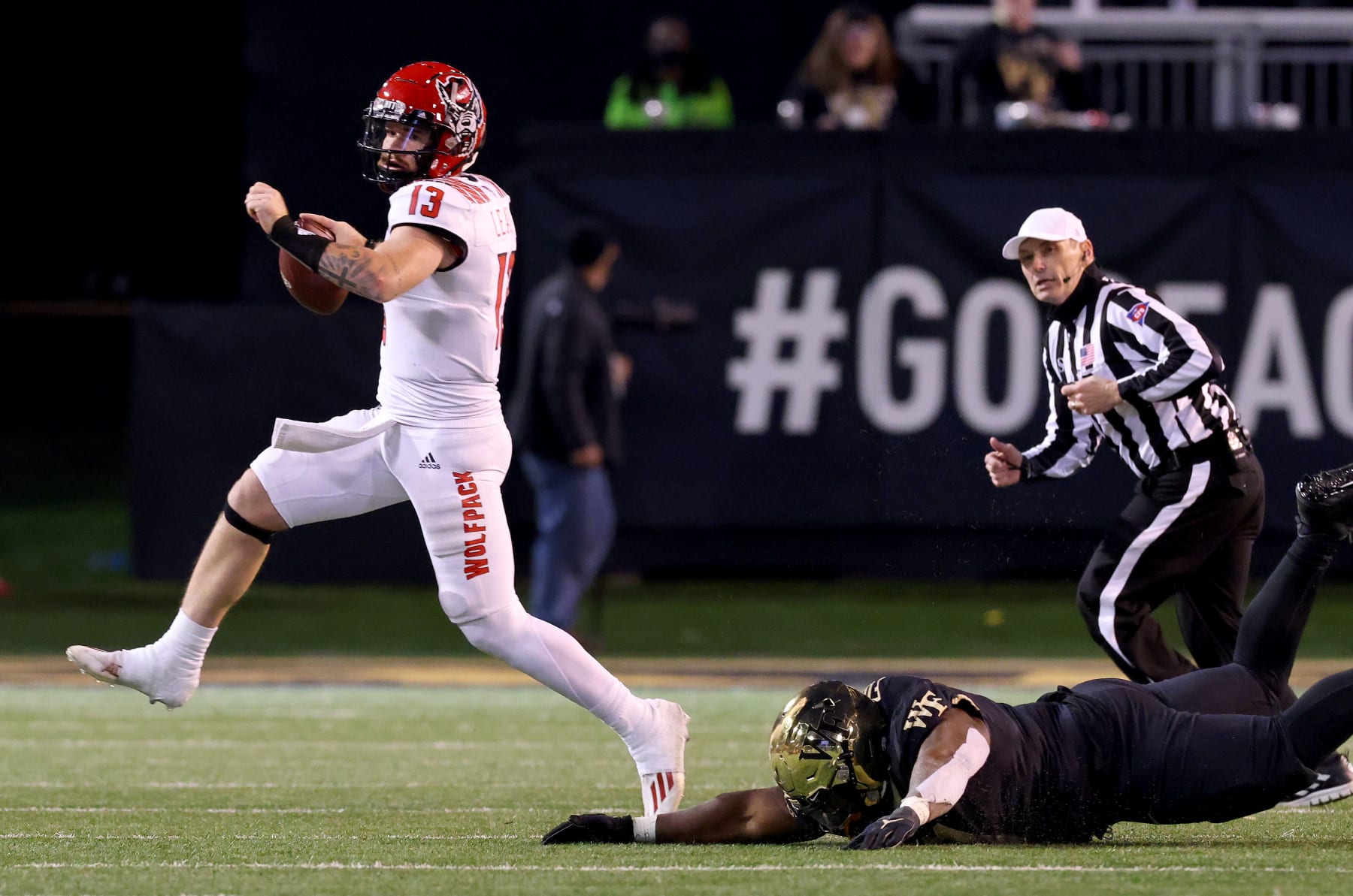 WINSTON-SALEM, NORTH CAROLINA - NOVEMBER 13: Devin Leary #13 of the North Carolina State Wolfpack rolls out under pressure from Miles Fox #11 of the Wake Forest Demon Deacons during the second half of their game at Truist Field on November 13, 2021 in Winston-Salem, North Carolina. Wake Forest won 45-42. (Photo by Grant Halverson/Getty Images)