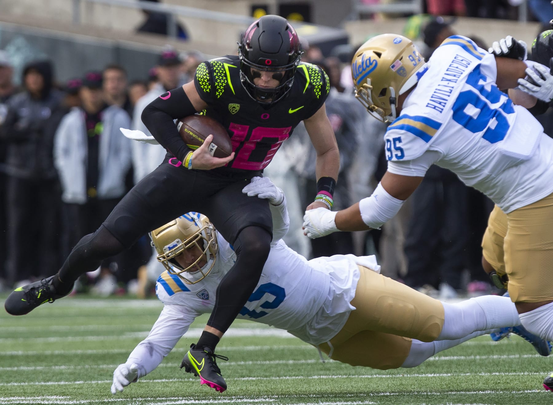 Oregon's Bo Nix, left, rushes against UCLA's Laiatu Latu, bottom and Sitiveni Havili-Kaufusi, right, during the second half in an NCAA college football game Saturday, Oct. 22, 2022, in Eugene, Ore. (AP Photo/Chris Pietsch)