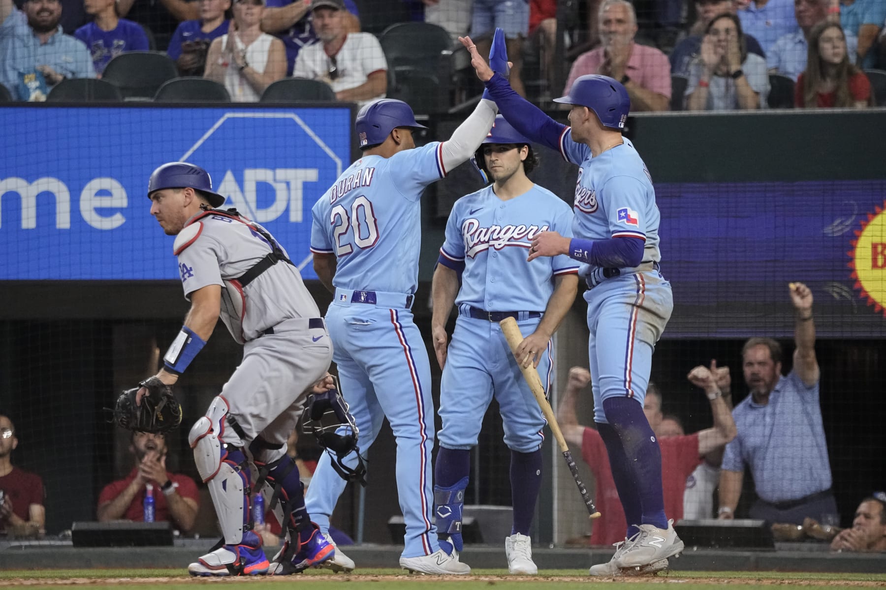 Ezequiel Duran (20) y Brad Miller, derecha, de los Rangers de Texas, celebran después de anotar con doble de Leody Taveras durante la tercera entrada del juego de béisbol en contra de los Dodgers de Los Ángeles, el domingo 23 de julio de 2023, en Arlington, Texas. (AP Foto/Sam Hodde)
