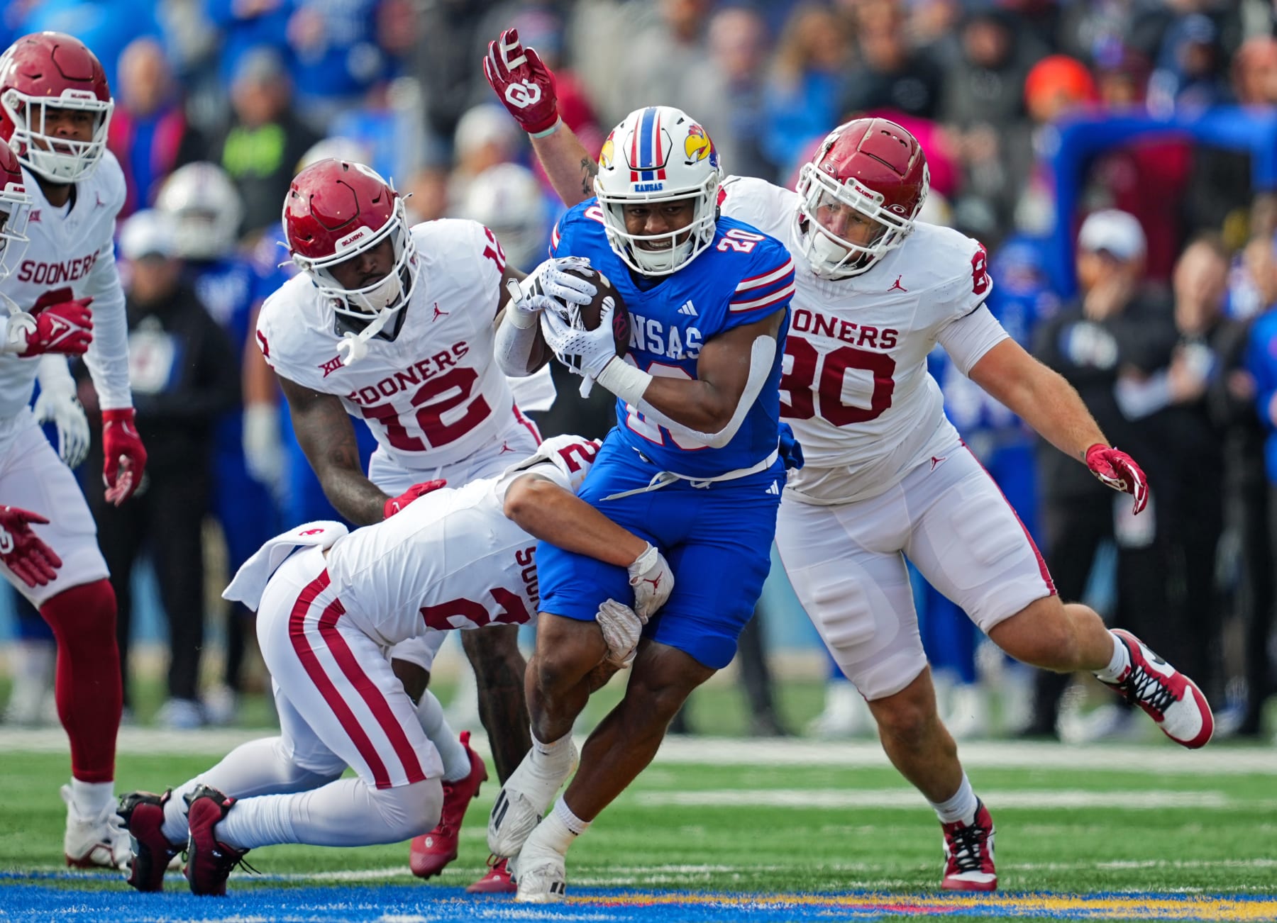 LAWRENCE, KANSAS - OCTOBER 28: Running back Daniel Hishaw Jr. #20 of the Kansas Jayhawks is tackled by defensive back Billy Bowman Jr. #2, defensive back Key Lawrence #12, and defensive lineman Rondell Bothroyd #80 of the Oklahoma Sooners during the first half at David Booth Kansas Memorial Stadium on October 28, 2023 in Lawrence, Kansas. (Photo by Jay Biggerstaff/Getty Images)