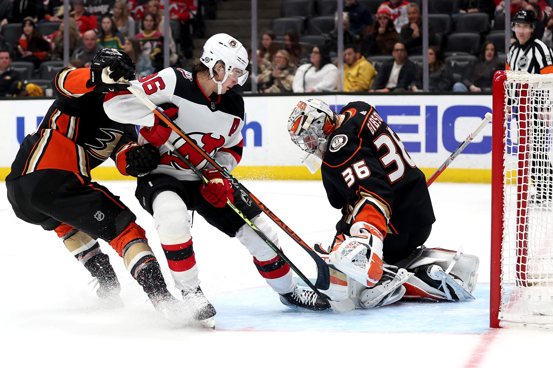 New Jersey Devils center Jack Hughes (center) and Anaheim Ducks goaltender John Gibson.