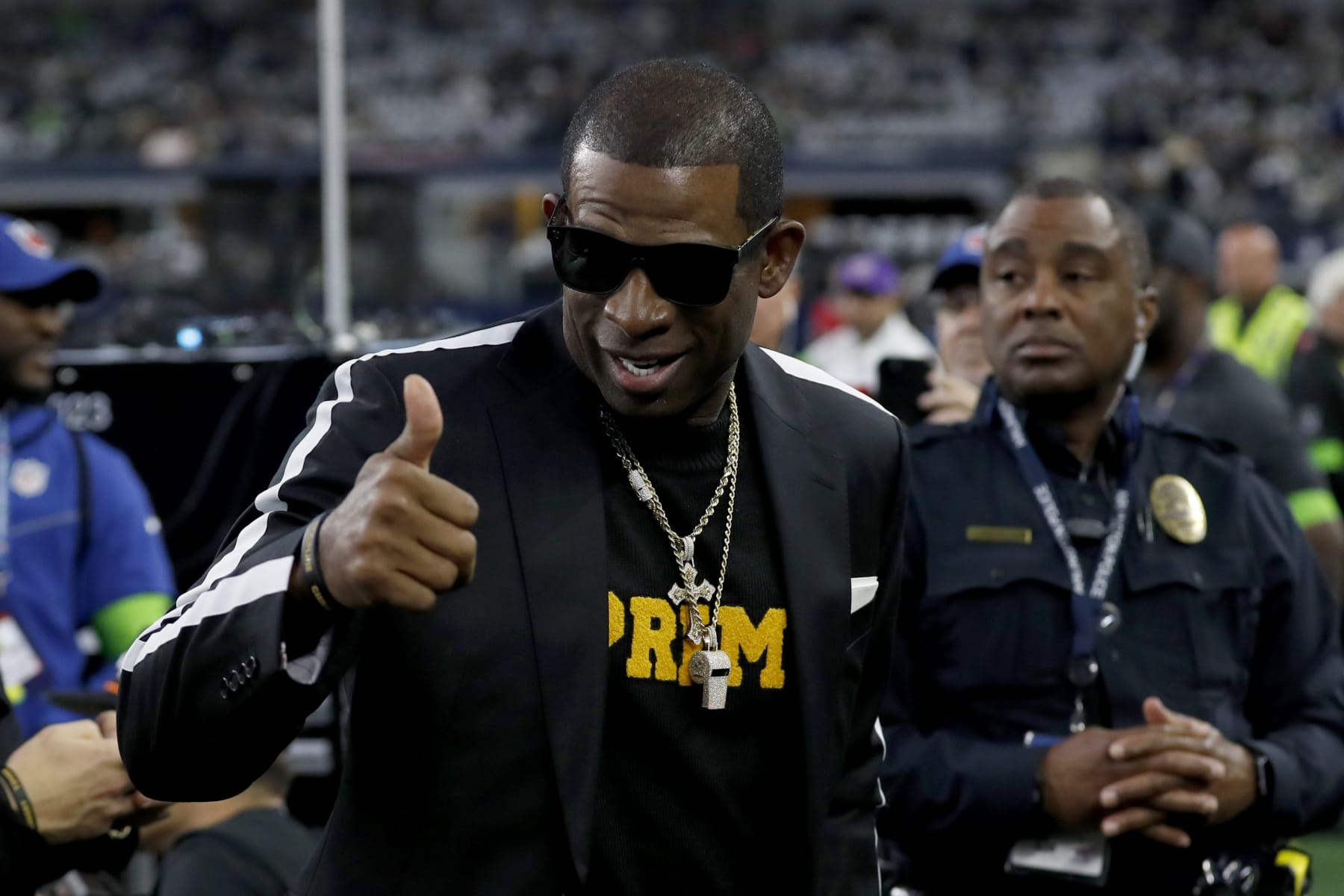 Colorado head football coach Deion Sanders, talks with persons on the sideline before the first half of an NFL football game between the Seattle Seahawks and Dallas Cowboys in Arlington, Texas, Thursday, Nov. 30, 2023. (AP Photo/Roger Steinman)
