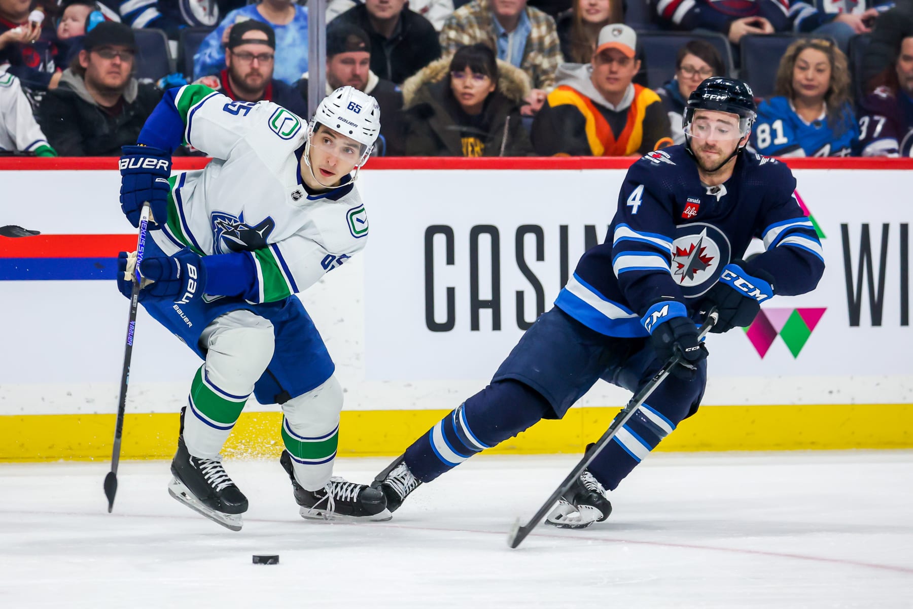 WINNIPEG, CANADA - JANUARY 08: Ilya Mikheyev #65 of the Vancouver Canucks plays the puck away from Neal Pionk #4 of the Winnipeg Jets during second period action at Canada Life Centre on January 08, 2023 in Winnipeg, Manitoba, Canada. (Photo by Jonathan Kozub/NHLI via Getty Images)