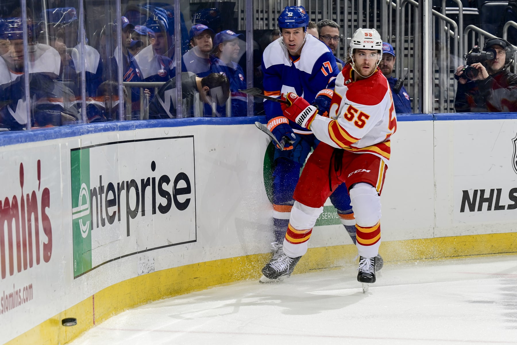 ELMONT, NEW YORK - FEBRUARY 10: Matt Martin #17 of the New York Islanders and Noah Hanifin #55 of the Calgary Flames pursue the puck during the third period at UBS Arena on February 10, 2024 in Elmont, New York. (Photo by Steven Ryan/NHLI via Getty Images)