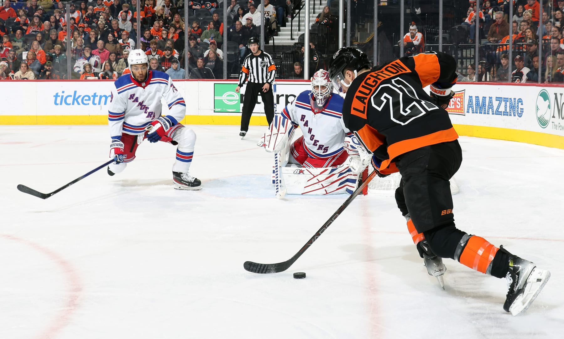 PHILADELPHIA, PENNSYLVANIA - NOVEMBER 24: Scott Laughton #21 of the Philadelphia Flyers skates the puck along the goal line against K Andre Miller #79 and Igor Shesterkin #31 of the New York Rangers at the Wells Fargo Center on November 24, 2023 in Philadelphia, Pennsylvania. (Photo by Len Redkoles/NHLI via Getty Images)