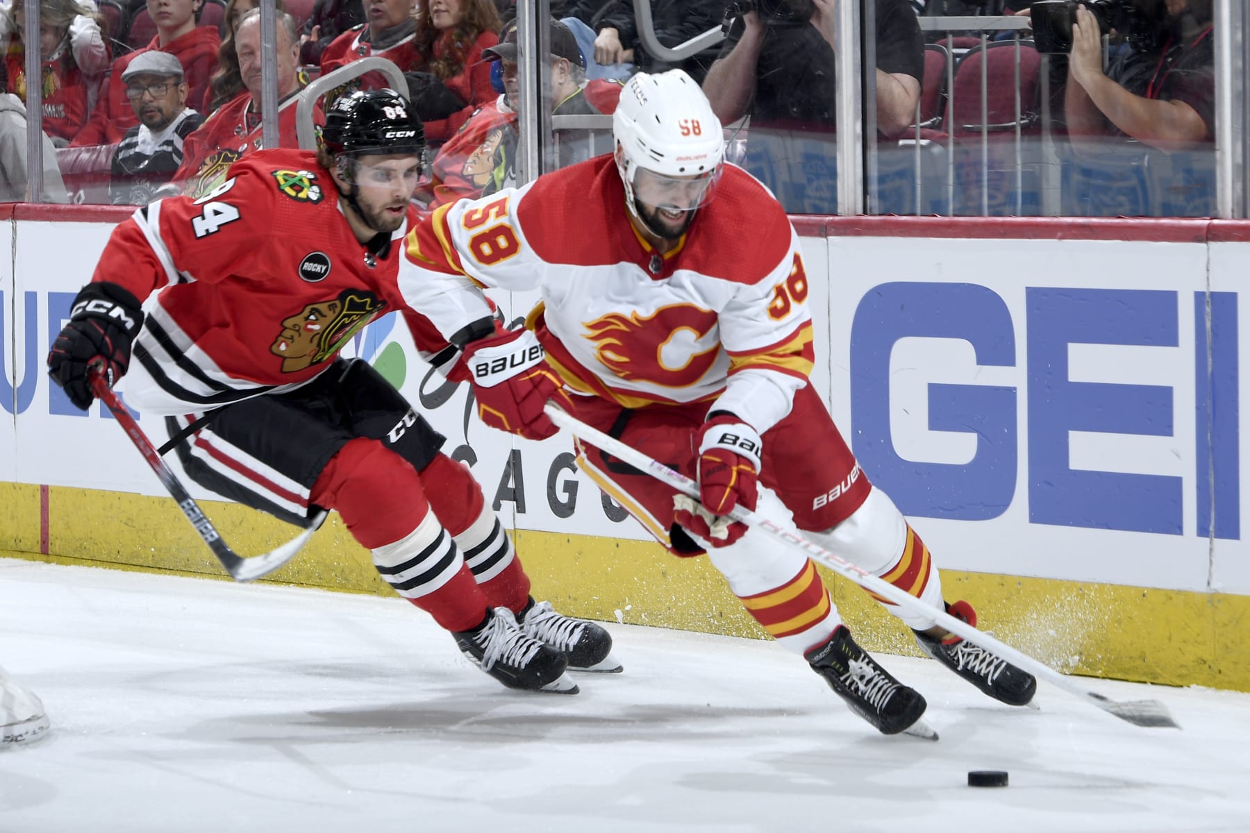 CHICAGO, ILLINOIS - MARCH 26: Oliver Kylington #58 of the Calgary Flames approaches the puck ahead of Landon Slaggert #84 of the Chicago Blackhawks in the third period at the United Center on March 26, 2024 in Chicago, Illinois. (Photo by Bill Smith/NHLI via Getty Images)