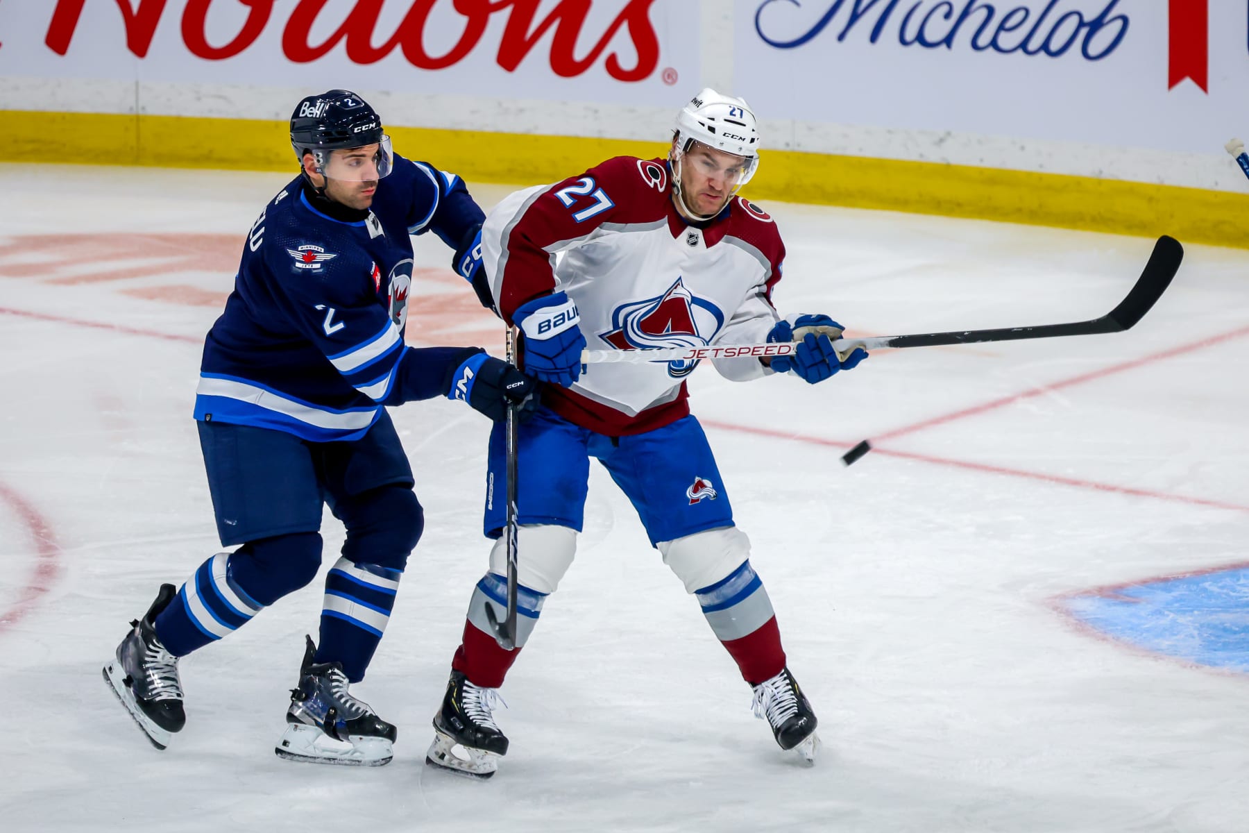 WINNIPEG, CANADA - DECEMBER 16: Jonathan Drouin #27 of the Colorado Avalanche and Dylan DeMelo #2 of the Winnipeg Jets keep their eyes on the puck during third period action at Canada Life Centre on December 16, 2023 in Winnipeg, Manitoba, Canada. (Photo by Jonathan Kozub/NHLI via Getty Images)