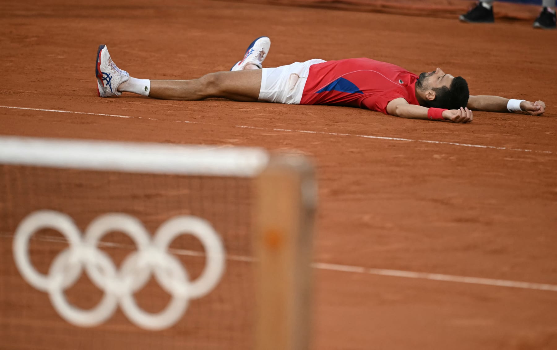 Serbia's Novak Djokovic falls to the ground as he reacts to beating Italy's Lorenzo Musetti during their men's singles semi-final tennis match on Court Philippe-Chatrier at the Roland-Garros Stadium during the Paris 2024 Olympic Games, in Paris on August 2, 2024. (Photo by CARL DE SOUZA / AFP) (Photo by CARL DE SOUZA/AFP via Getty Images)