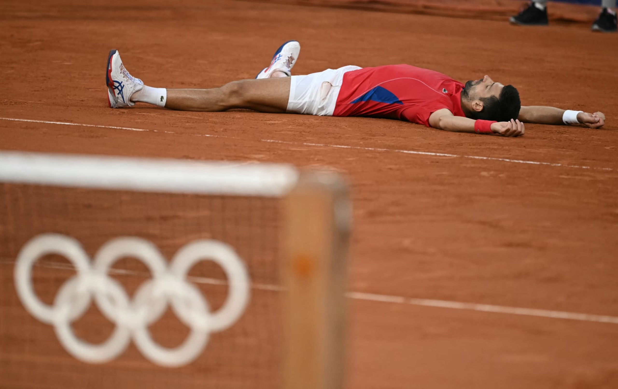 Serbia's Novak Djokovic falls to the ground as he reacts to beating Italy's Lorenzo Musetti during their men's singles semi-final tennis match on Court Philippe-Chatrier at the Roland-Garros Stadium during the Paris 2024 Olympic Games, in Paris on August 2, 2024. (Photo by CARL DE SOUZA / AFP) (Photo by CARL DE SOUZA/AFP via Getty Images)