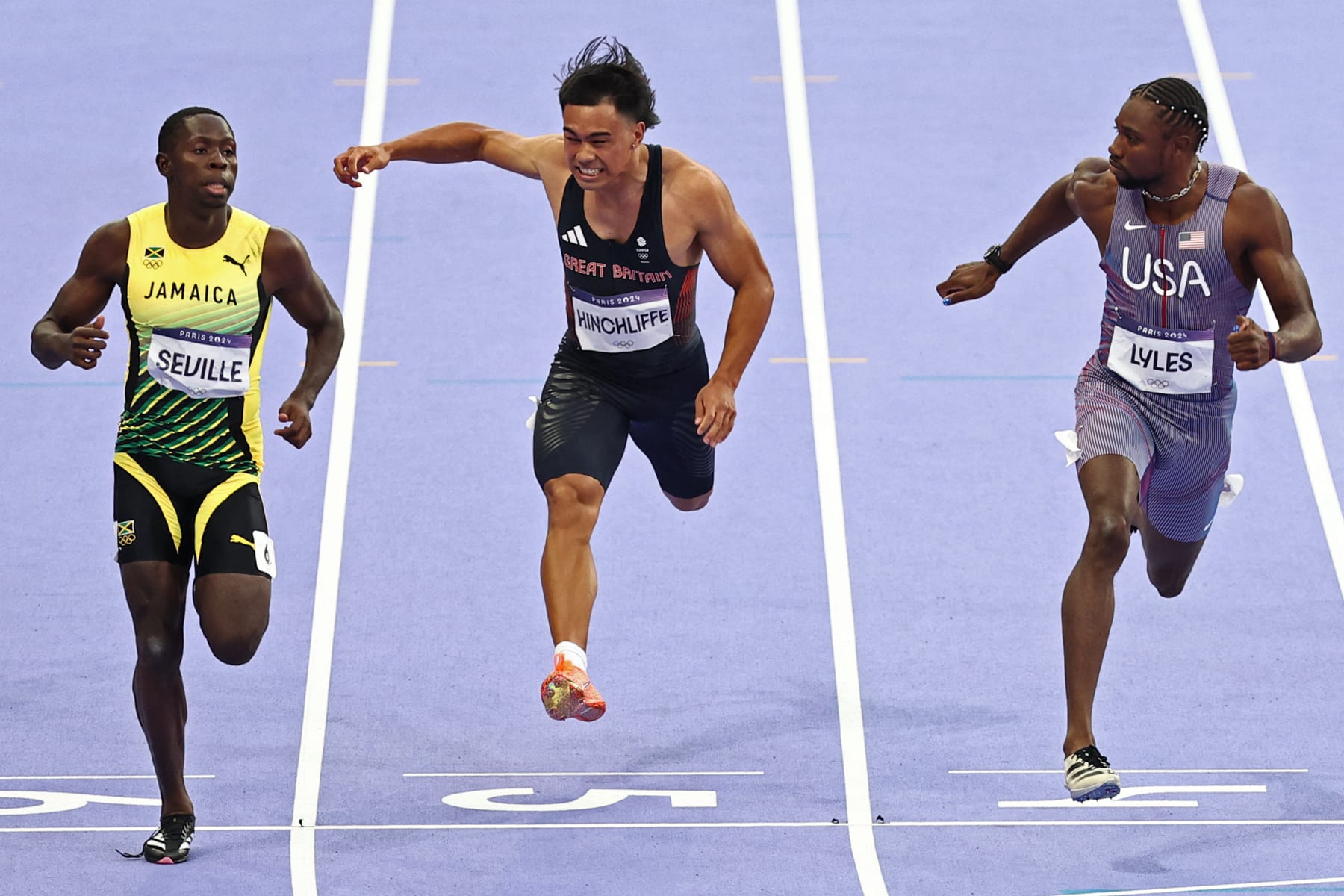 Jamaica's Oblique Seville (L) crosses the finish line ahead of Britain's Louie Hinchliffe and US' Noah Lyles in the men's 100m semi-final of the athletics event at the Paris 2024 Olympic Games at Stade de France in Saint-Denis, north of Paris, on August 4, 2024. (Photo by Anne-Christine POUJOULAT / AFP) (Photo by ANNE-CHRISTINE POUJOULAT/AFP via Getty Images)