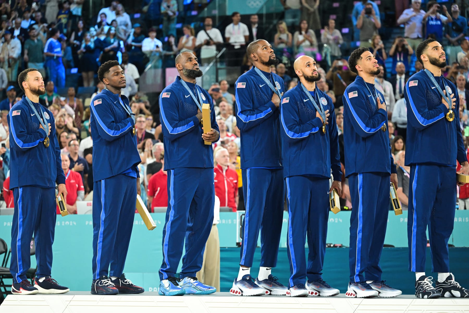 Gold medallists (From L) USA's #04 Stephen Curry, USA's #05 Anthony Edwards, USA's #06 LeBron James, USA's #07 Kevin Durant, USA's #08 Derrick White, USA's #09 Tyrese Haliburton and USA's #10 Jayson Tatum stand at attention during their national anthem, on the podium after the men's Gold Medal basketball match between France and USA during the Paris 2024 Olympic Games at the Bercy  Arena in Paris on August 10, 2024. (Photo by Damien MEYER / AFP) (Photo by DAMIEN MEYER/AFP via Getty Images)