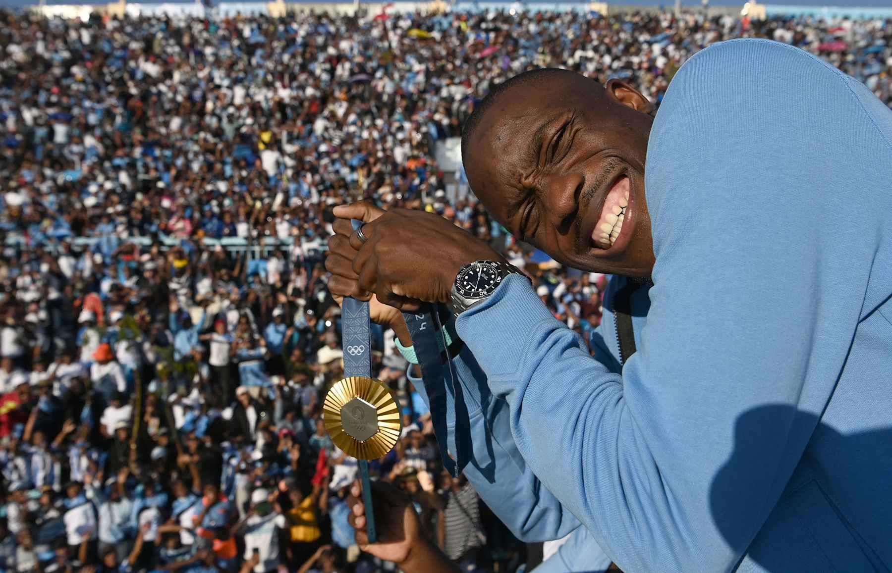 Olympic gold medallist, Botswana's Letsile Tebogo, who won the men's 200m athletics event during the Paris 2024 Olympic Games, holds his gold medal as he arrives on an open bus at the Botswana national Stadium during a welcoming ceremony in Gaborone on 13 August 2024. Botswana gave a rapturous welcome to Letsile Tebogo on Tuesday as the sprinter returned home with the southern African country's first ever Olympic gold medal. Families with children, elderly people and young supporters waved Botswana's sky blue, white and black national flag as the Olympic team landed back in the capital Gaborone. Hundreds of supporters had gathered at the small airport, benefiting from an impromptu half-day holiday declared by President Mokgweetsi Masisi to celebrate Tebogo's success. (Photo by Monirul Bhuiyan / AFP) (Photo by MONIRUL BHUIYAN/AFP via Getty Images)