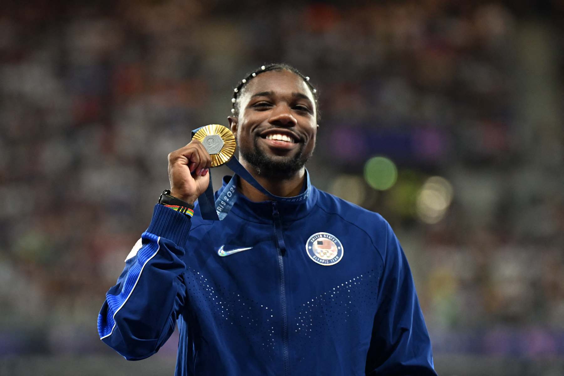 Gold medallist US' Noah Lyles celebrates on the podium during the victory ceremony for the men's 100m athletics event during the Paris 2024 Olympic Games at Stade de France in Saint-Denis, north of Paris, on August 5, 2024. (Photo by MARTIN BERNETTI / AFP) (Photo by MARTIN BERNETTI/AFP via Getty Images)