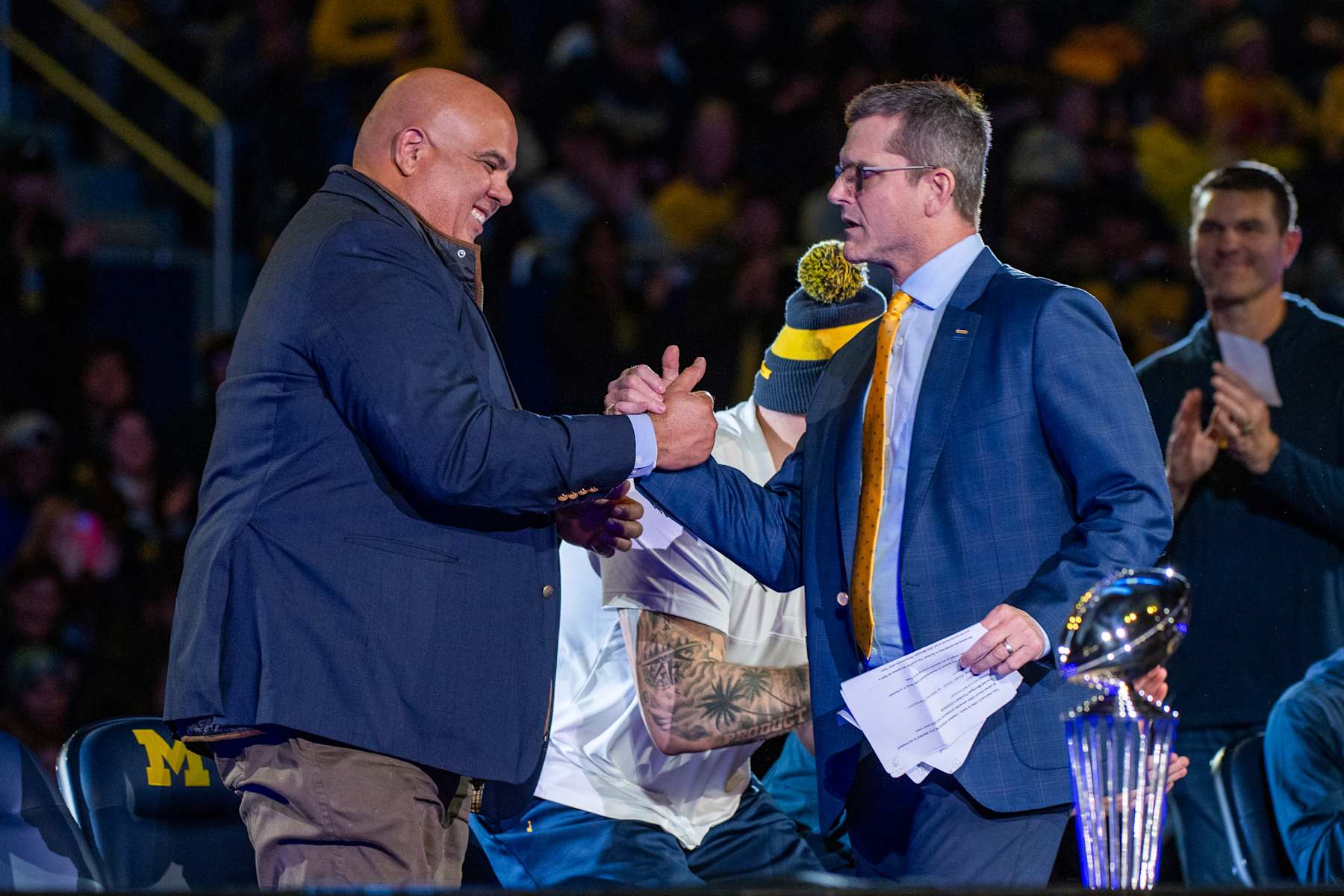 ANN ARBOR, MICHIGAN - JANUARY 13: Athletic Director Warde Manuel (L) and Head Football Coach Jim Harbaugh (R) of the Michigan Wolverines shake hands onstage during the National Championship Celebration at Crisler Center on January 13, 2024 in Ann Arbor, Michigan. (Photo by Aaron J. Thornton/Getty Images)