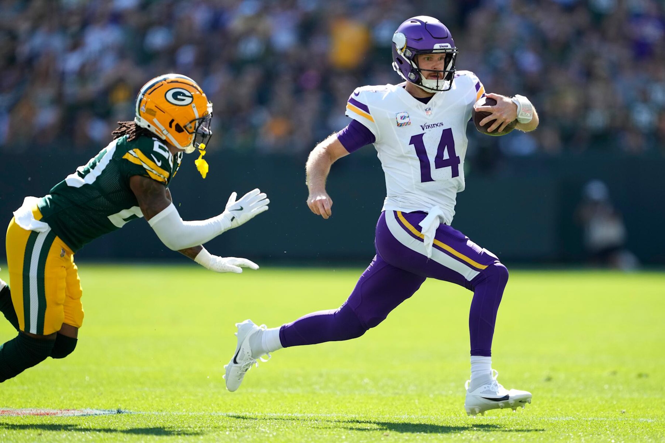 GREEN BAY, WISCONSIN - SEPTEMBER 29: Sam Darnold #14 of the Minnesota Vikings carries the ball past Javon Bullard #20 of the Green Bay Packers during the first half at Lambeau Field on September 29, 2024 in Green Bay, Wisconsin. (Photo by Patrick McDermott/Getty Images)