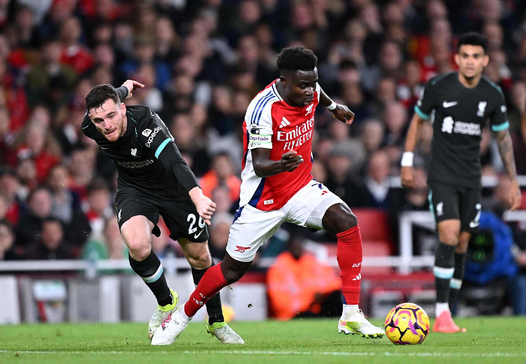 LONDON, ENGLAND - OCTOBER 27: Bukayo Saka of Arsenal runs with the ball whilst under pressure from Andrew Robertson of Liverpool during the Premier League match between Arsenal FC and Liverpool FC at Emirates Stadium on October 27, 2024 in London, England. (Photo by David Price/Arsenal FC via Getty Images)