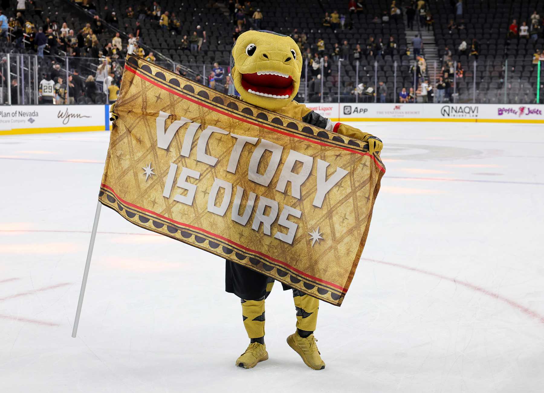 LAS VEGAS, NEVADA - OCTOBER 28: The Vegas Golden Knights mascot Chance the Golden Gila Monster holds a flag with the message "Victory is ours" after the team's 5-0 win over the Calgary Flames at T-Mobile Arena on October 28, 2024 in Las Vegas, Nevada. (Photo by Ethan Miller/Getty Images)