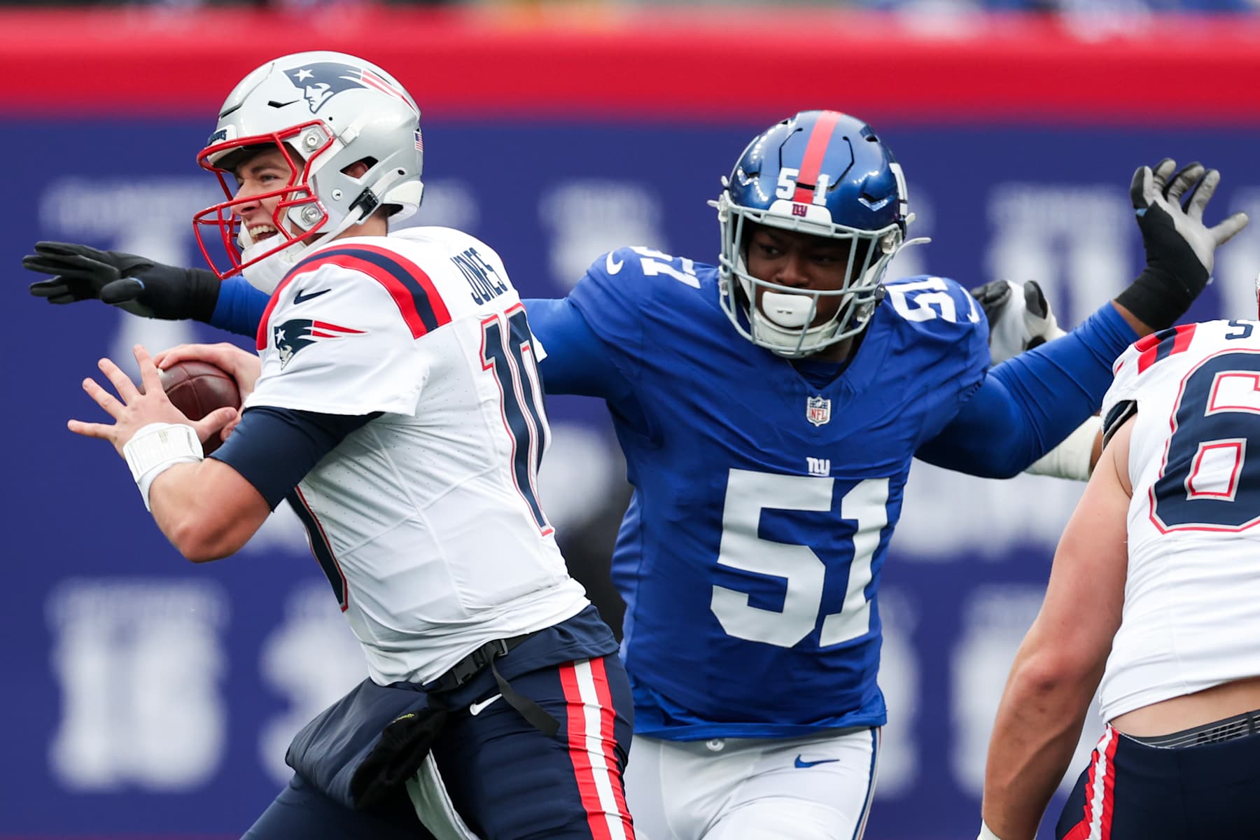 EAST RUTHERFORD, NEW JERSEY - NOVEMBER 26: Mac Jones #10 of the New England Patriots attempts a pass while pressured by Azeez Ojulari #51 of the New York Giants during the first quarter at MetLife Stadium on November 26, 2023 in East Rutherford, New Jersey. (Photo by Al Bello/Getty Images)