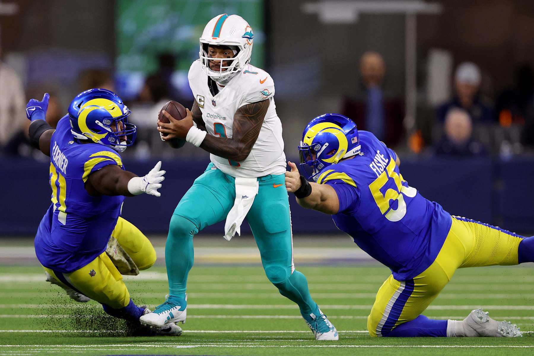 INGLEWOOD, CALIFORNIA - NOVEMBER 11: Tua Tagovailoa #1 of the Miami Dolphins break a tackle against Kobie Turner #91 and Braden Fiske #55 of the Los Angeles Rams during the first quarter in the game at SoFi Stadium on November 11, 2024 in Inglewood, California. (Photo by Sean M. Haffey/Getty Images)