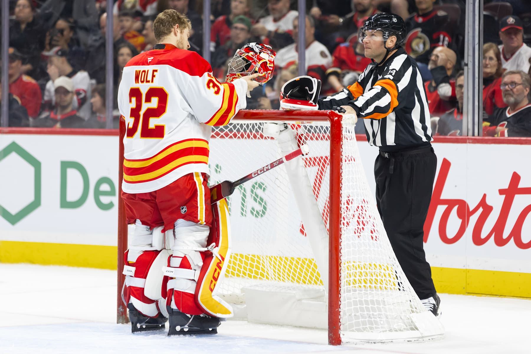 OTTAWA, ON - NOVEMBER 25: Referee Trevor Hanson (14) waits for Calgary Flames Goalie Dustin Wolf (32) to fix his mask during first period National Hockey League action between the Calgary Flames and Ottawa Senators on November 25, 2024, at Canadian Tire Centre in Ottawa, ON, Canada. (Photo by Richard A. Whittaker/Icon Sportswire via Getty Images)