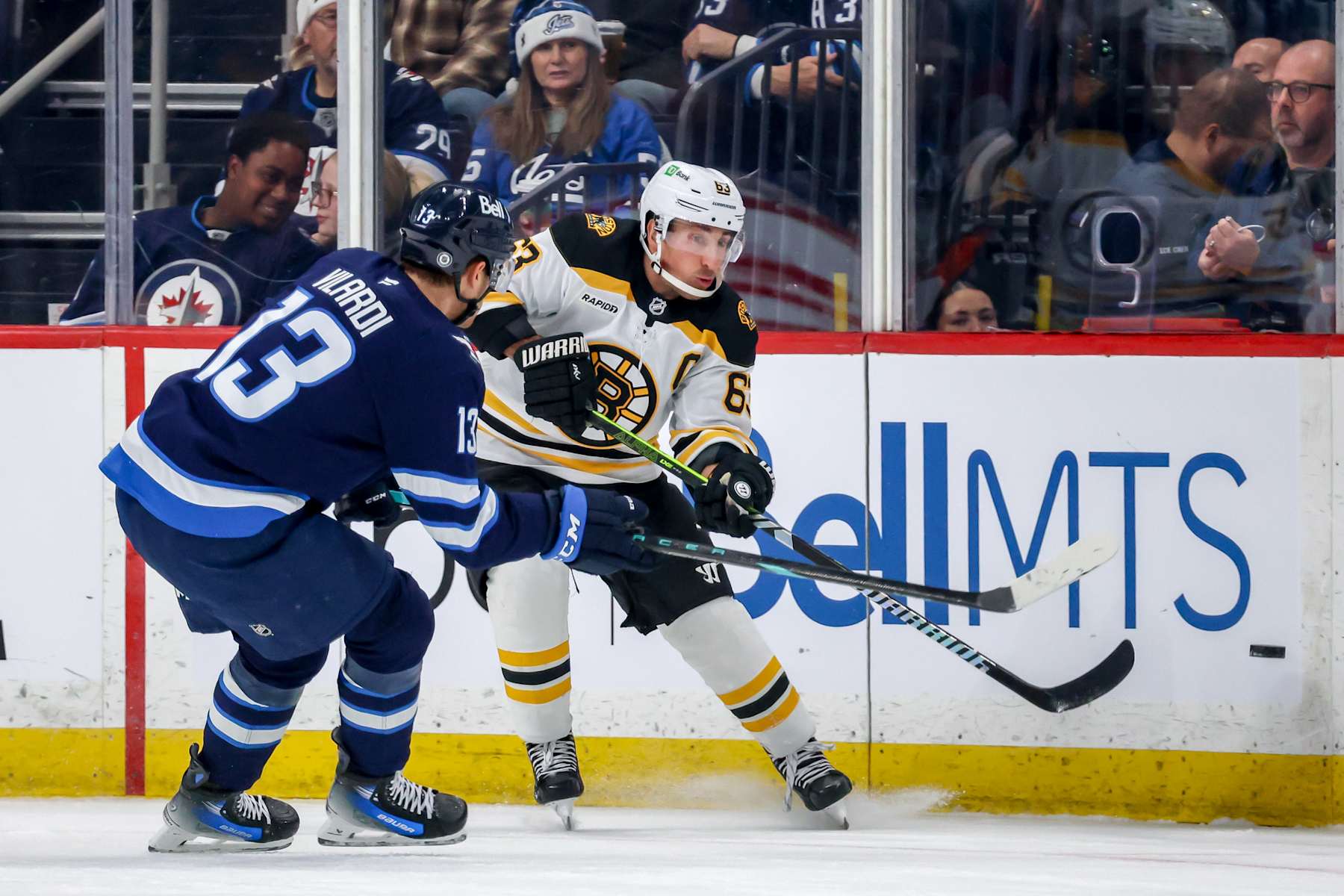 WINNIPEG, CANADA - DECEMBER 10: Brad Marchand #63 of the Boston Bruins chips the puck past Gabriel Vilardi #13 of the Winnipeg Jets during first period action at the Canada Life Centre on December 10, 2024 in Winnipeg, Manitoba, Canada. (Photo by Jonathan Kozub/NHLI via Getty Images)