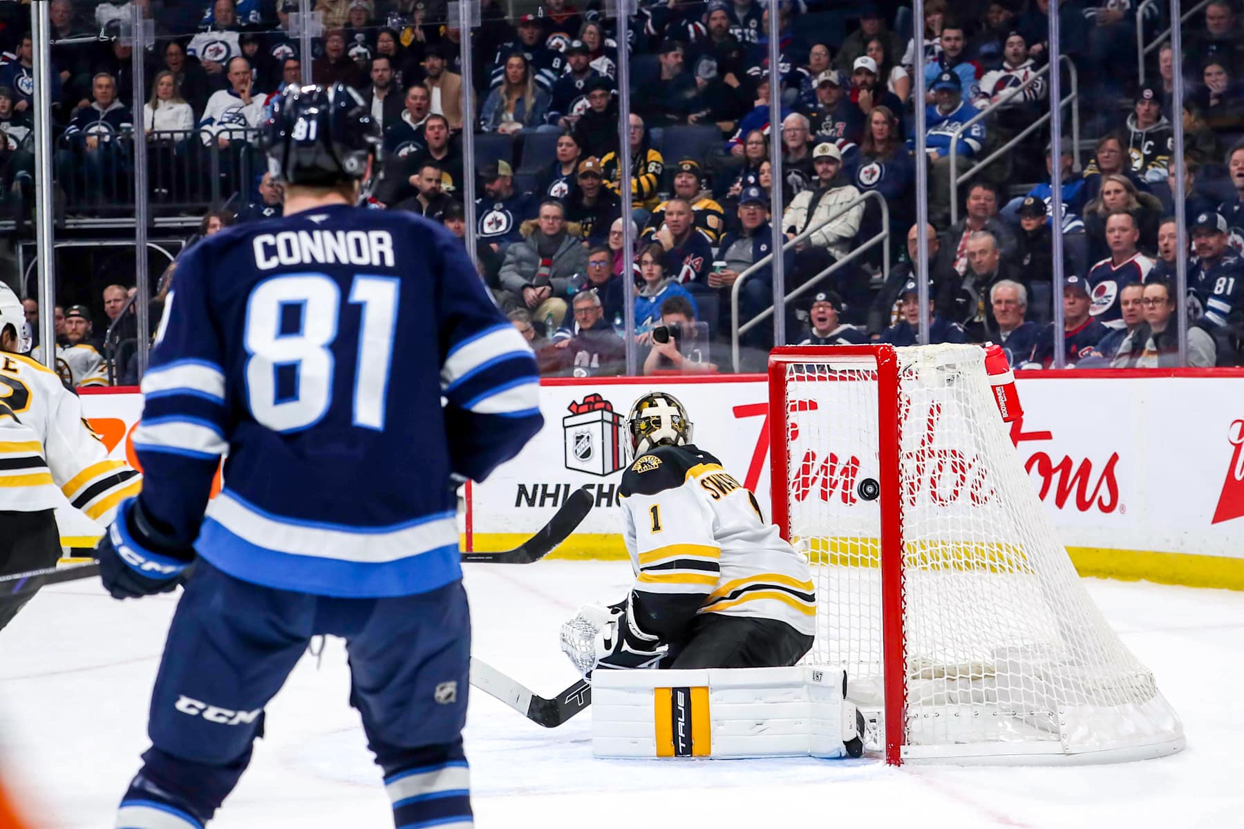 WINNIPEG, CANADA - DECEMBER 10: Kyle Connor #81 of the Winnipeg Jets watches as a shot by teammate Mark Scheifele #55 (not seen) gets behind goaltender Jeremy Swayman #1 of the Boston Bruins for a first period goal at the Canada Life Centre on December 10, 2024 in Winnipeg, Manitoba, Canada. (Photo by Darcy Finley/NHLI via Getty Images)