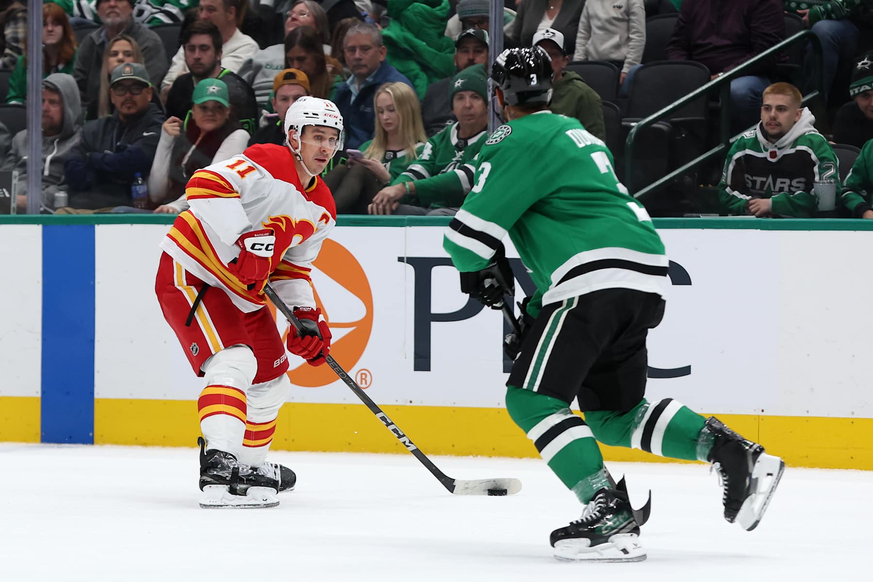 DALLAS, TEXAS - DECEMBER 08: Mikael Backlund #11 of the Calgary Flames skates with the puck against Mathew Dumba #3 of the Dallas Stars during the second period at American Airlines Center on December 08, 2024 in Dallas, Texas. (Photo by Sam Hodde/Getty Images)