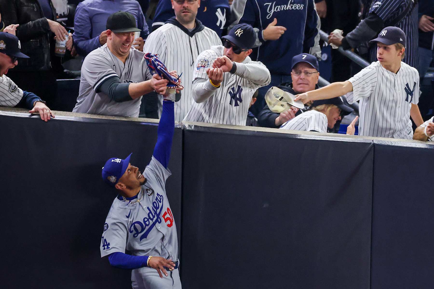 NEW YORK, NEW YORK - OCTOBER 29:  Fans Austin Capobianco (L) and John Peter (R) interfere with Mookie Betts #50 of the Los Angeles Dodgers as he attempts to catch a fly ball in foul territory during the first inning of Game Four of the 2024 World Series against the New York Yankees at Yankee Stadium on October 29, 2024 in the Bronx borough of New York City. The play resulted in an out. (Photo by Al Bello/Getty Images)