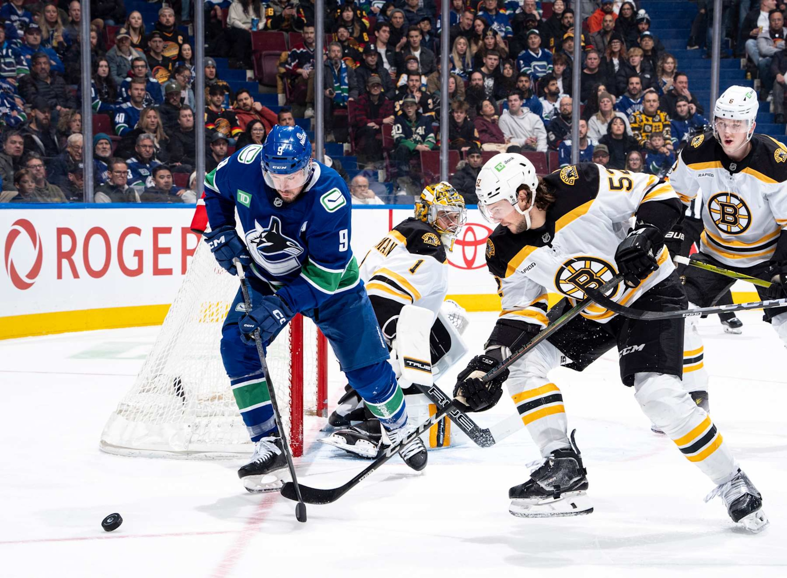 VANCOUVER, CANADA - DECEMBER 14:J.T. Miller #9 of the Vancouver Canucks and Andrew Peeke #52 of the Boston Bruins battle for the puck during the first period of their NHL game at Rogers Arena on December 14, 2024 in Vancouver, British Columbia, Canada.  (Photo by Jeff Vinnick/NHLI via Getty Images)