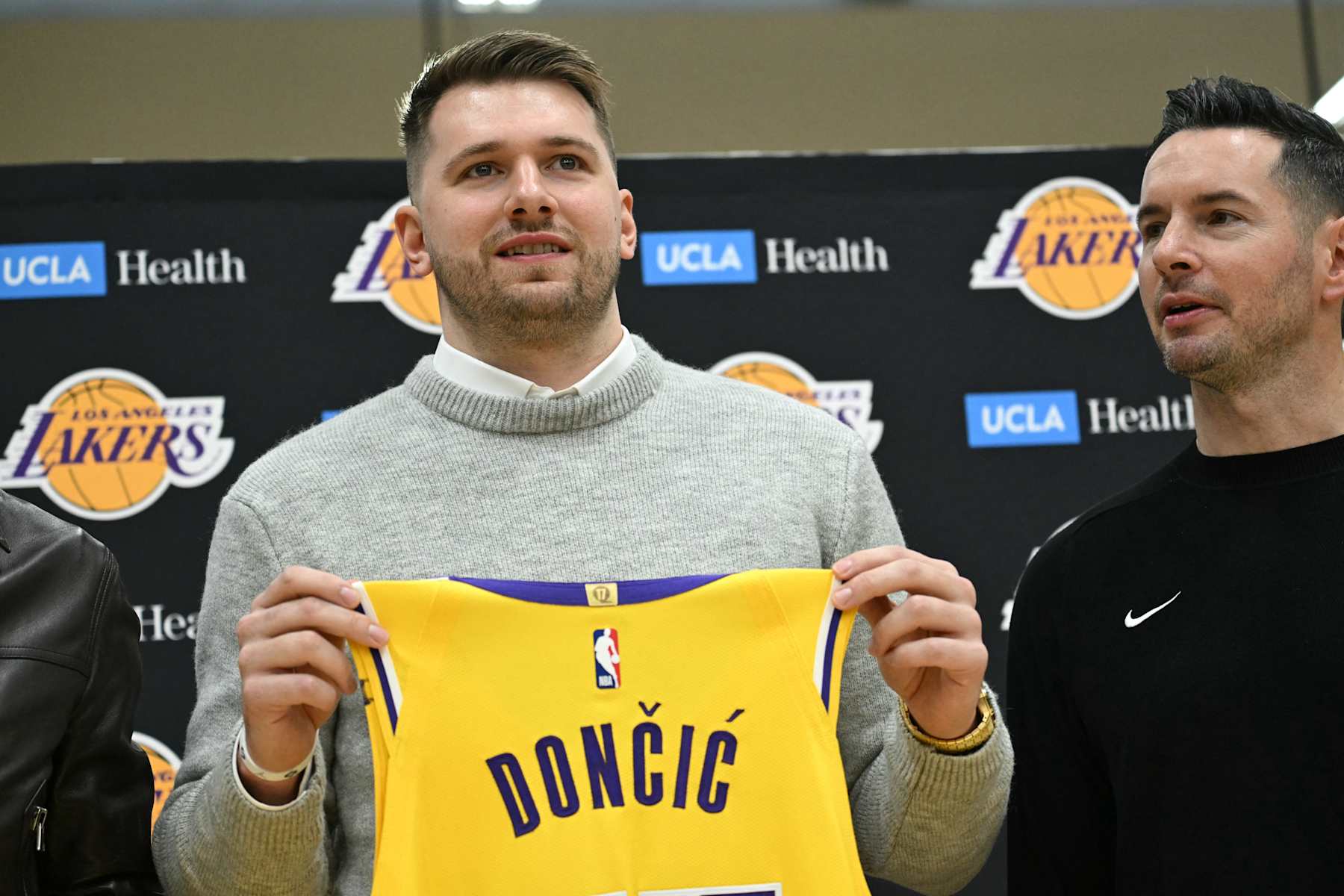 Slovenian basketball player Luka Doncic (L) holds up a jersey as he stands alongside Los Angeles Lakers head coach JJ Redick during a press conference introducing Doncic as the newest member of the Los Angeles Lakers, at the UCLA Health Training Center, in El Segundo, California on February 4, 2025. Slovenian star Luka Doncic said February 2, 2025 he thought he'd spend his entire NBA career in Dallas, thanking fans in Texas for making it feel like home a day after the Mavericks abruptly traded him to the Los Angeles Lakers. (Photo by Patrick T. Fallon / AFP) (Photo by PATRICK T. FALLON/AFP via Getty Images)          
