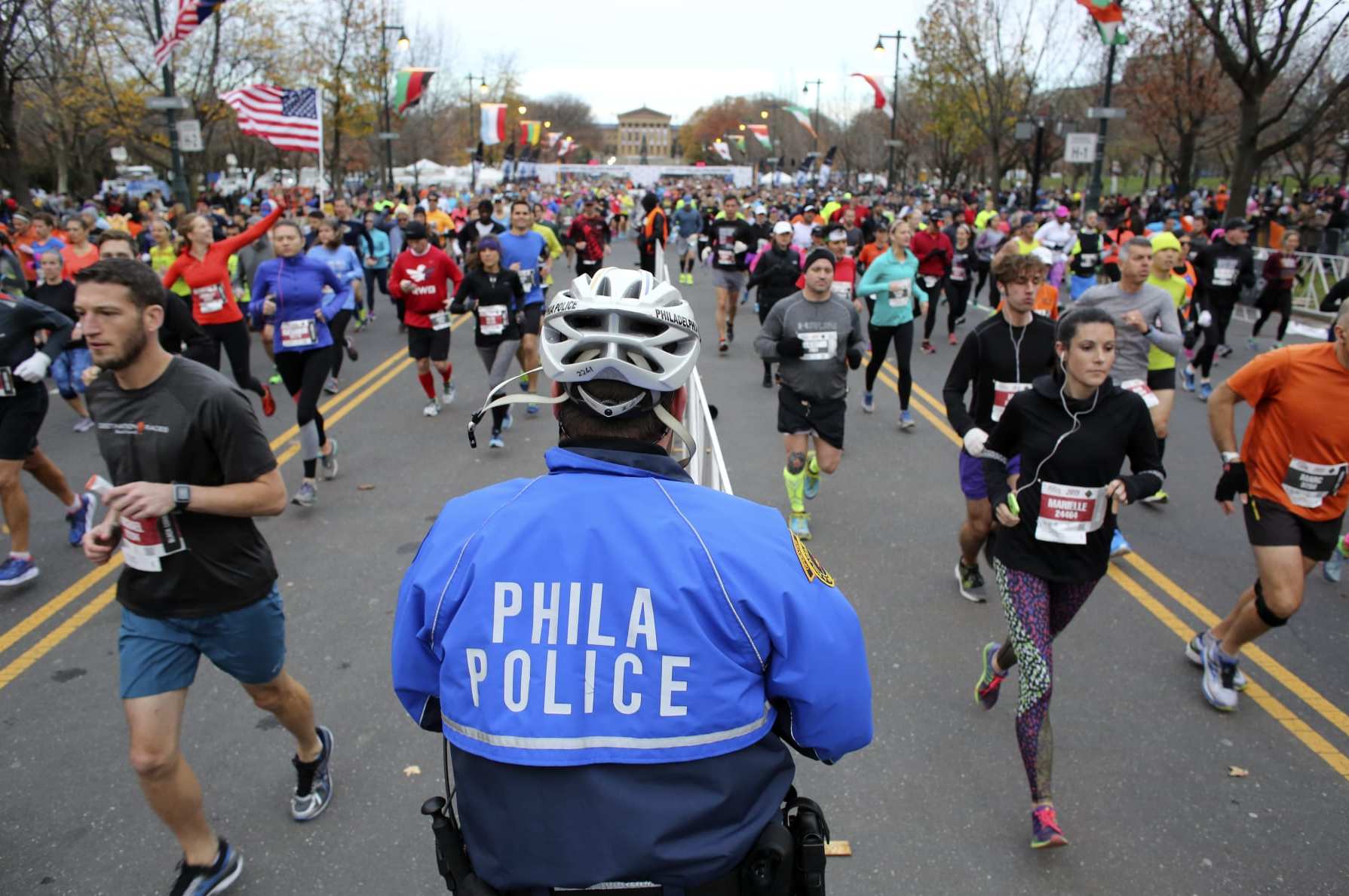 Philadelphia police Officer Andrew Schafer watches as runners make their way down the Benjamin Franklin Parkway in Philadelphia at the start of the Philadelphia Marathon, Sunday, Nov. 22, 2015. (AP Photo/ Joseph Kaczmarek)