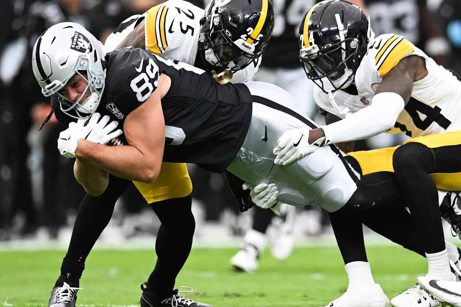 LAS VEGAS, NEVADA - OCTOBER 13: Brock Bowers #89 of the Las Vegas Raiders dives as he is tackled by DeShon Elliott #25 and Joey Porter Jr. #24 of the Pittsburgh Steelers in the first quarter of a game at Allegiant Stadium on October 13, 2024 in Las Vegas, Nevada. (Photo by Candice Ward/Getty Images)