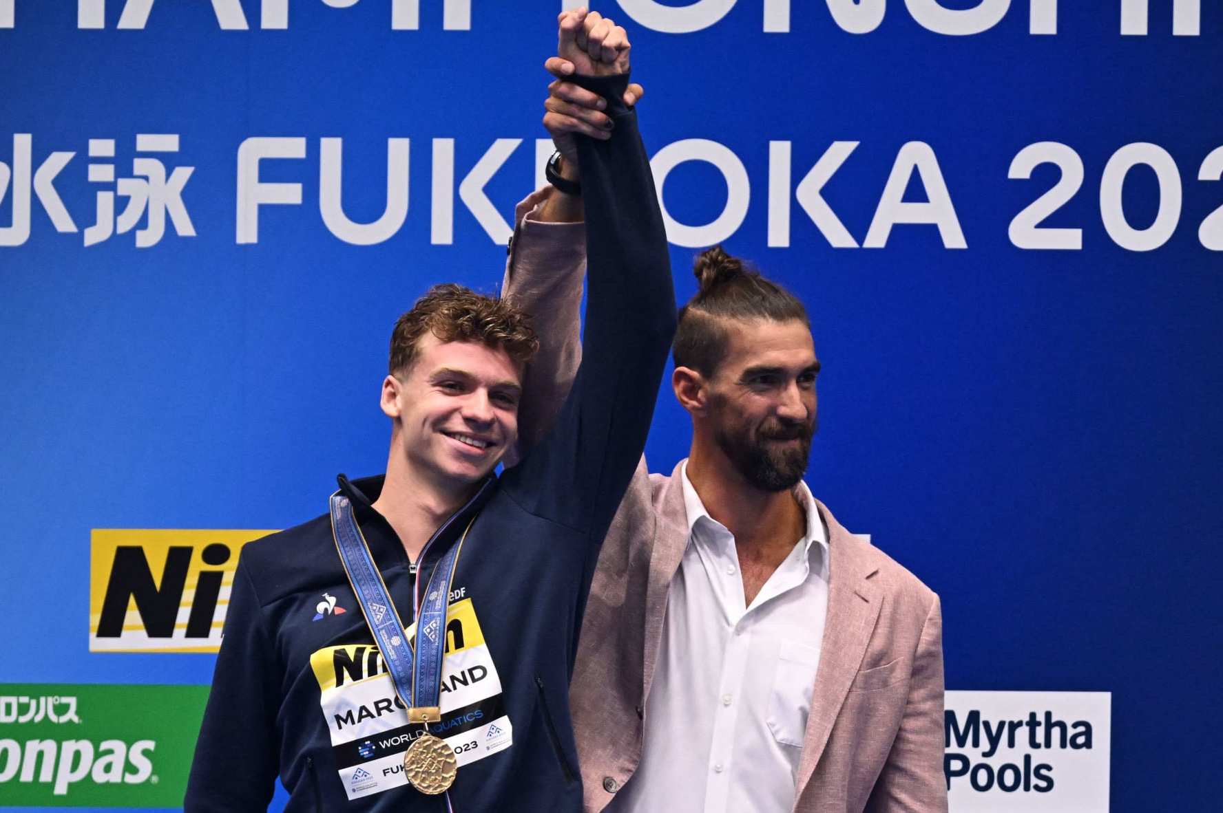 (L-R) Gold medallist France's Leon Marchand celebrates with former US swimmer Michael Phelps during the medals ceremony for men's 400m medley swimming event during the World Aquatics Championships in Fukuoka on July 23, 2023. (Photo by MANAN VATSYAYANA / AFP) (Photo by MANAN VATSYAYANA/AFP via Getty Images)