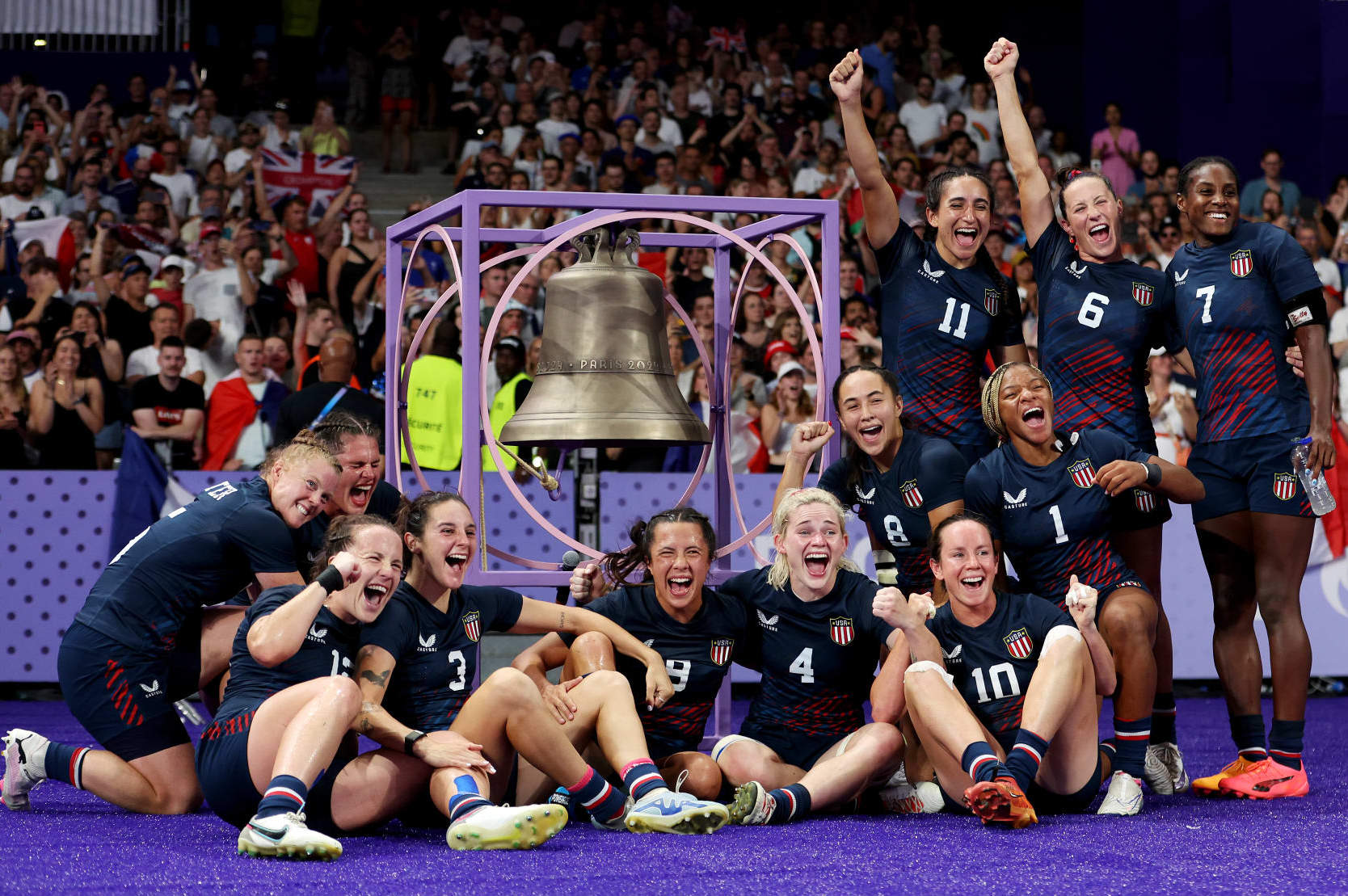 PARIS, FRANCE - JULY 29: Team United States celebrate victory as they pose for a photo with the Bell after the Women's Rugby Sevens Quarter Final match between Team Great Britain and Team United States on day three of the Olympic Games Paris 2024 at Stade de France on July 29, 2024 in Paris, France. (Photo by Michael Steele/Getty Images)