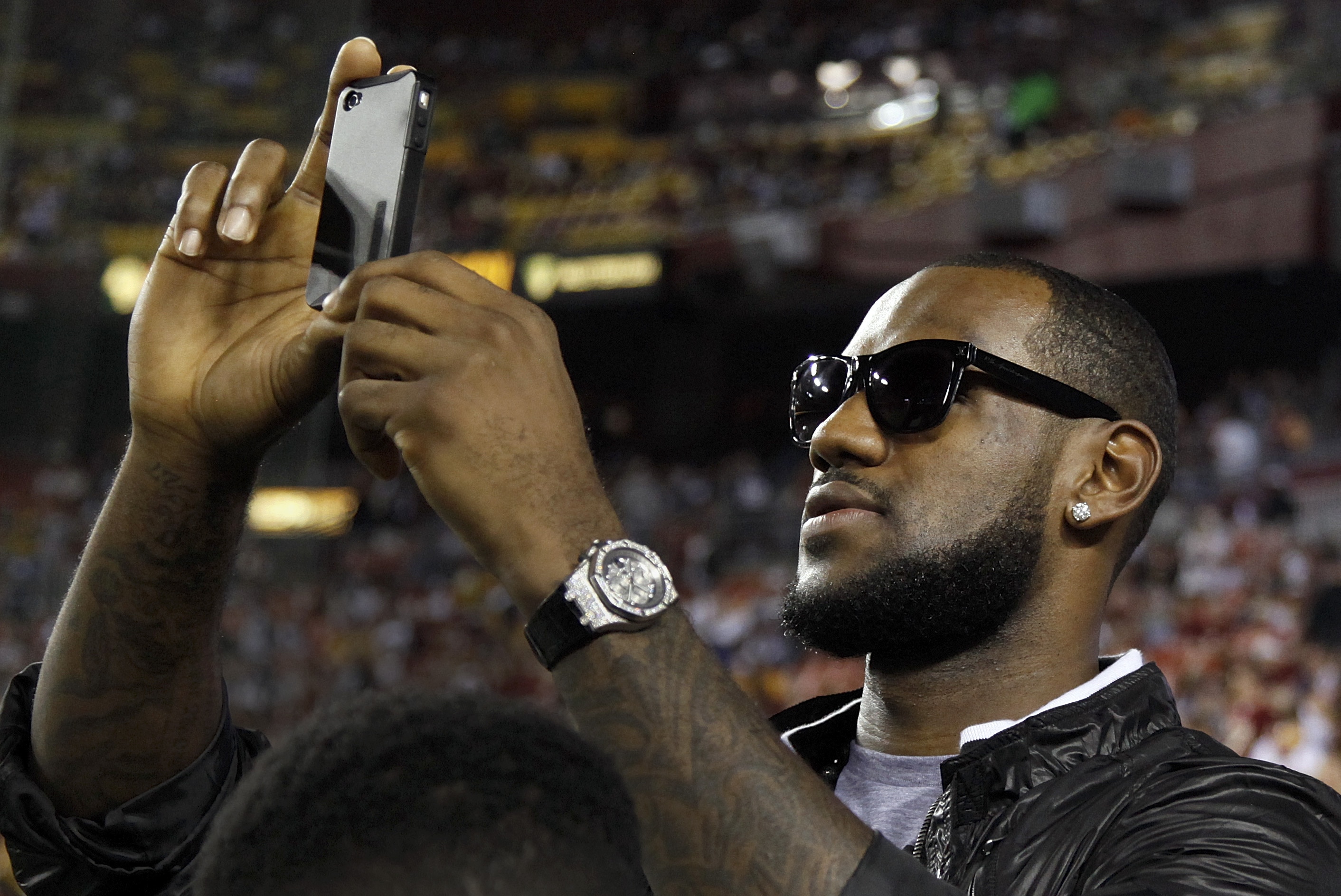 Basketball player LeBron James shoots a video with his cell phone from the sidelines before an NFL football game between the Dallas Cowboys and Washington Redskins in Landover, Md., on Sunday, Sept. 12, 2010. (AP Photo/Evan Vucci)